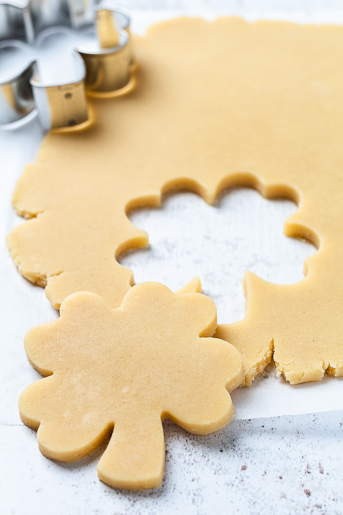 Shamrock cookie dough cutouts made with clover-shaped cookie cutter on floured surface.