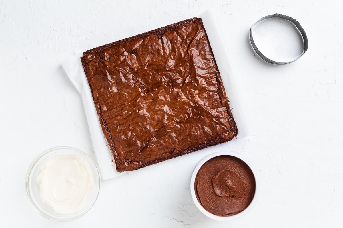 Brownie slab with bowls of chocolate and white frosting ready for decorating.