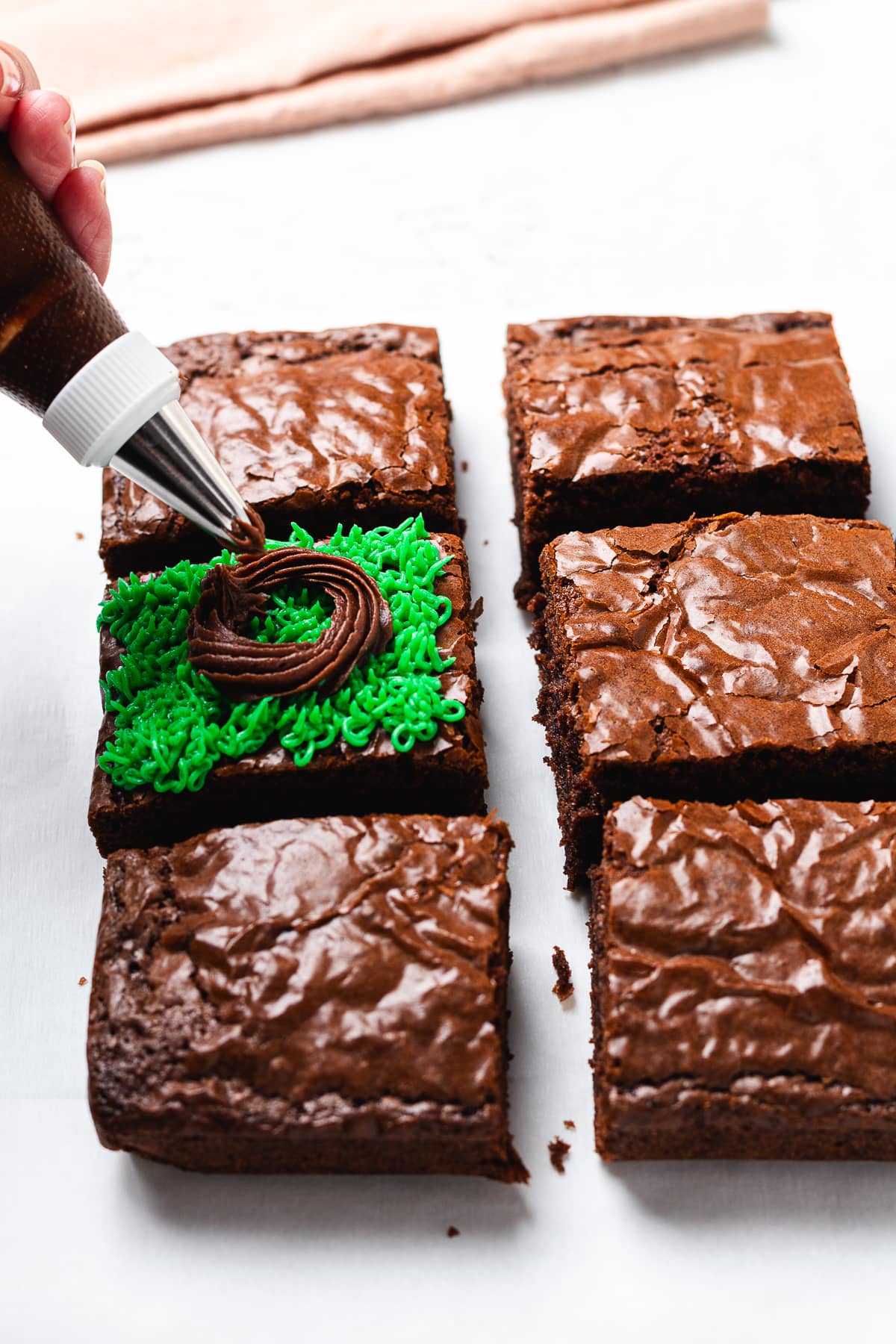 Adding chocolate frosting nest over green frosting grass on brownies.