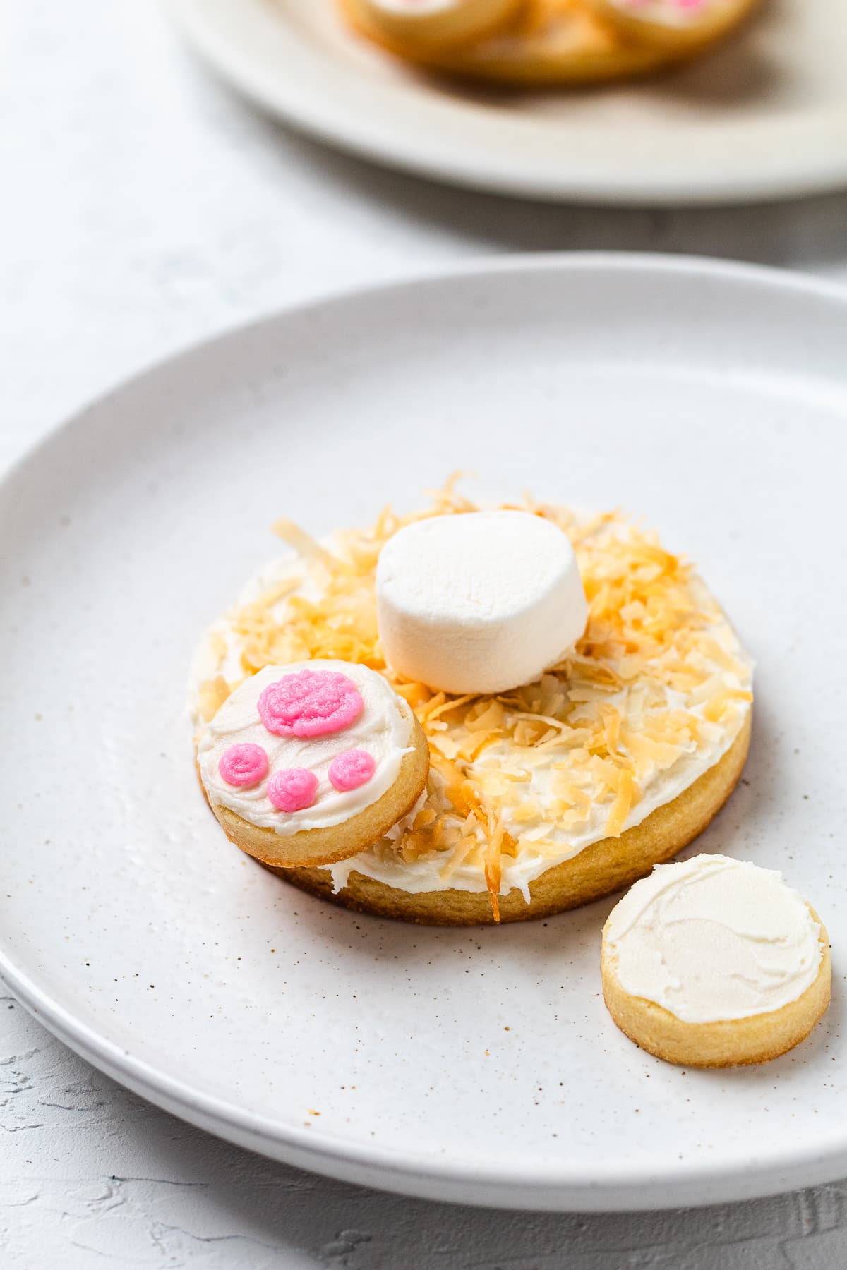 Partially assembled bunny butt cookie with marshmallow tail and one frosted paw attached.