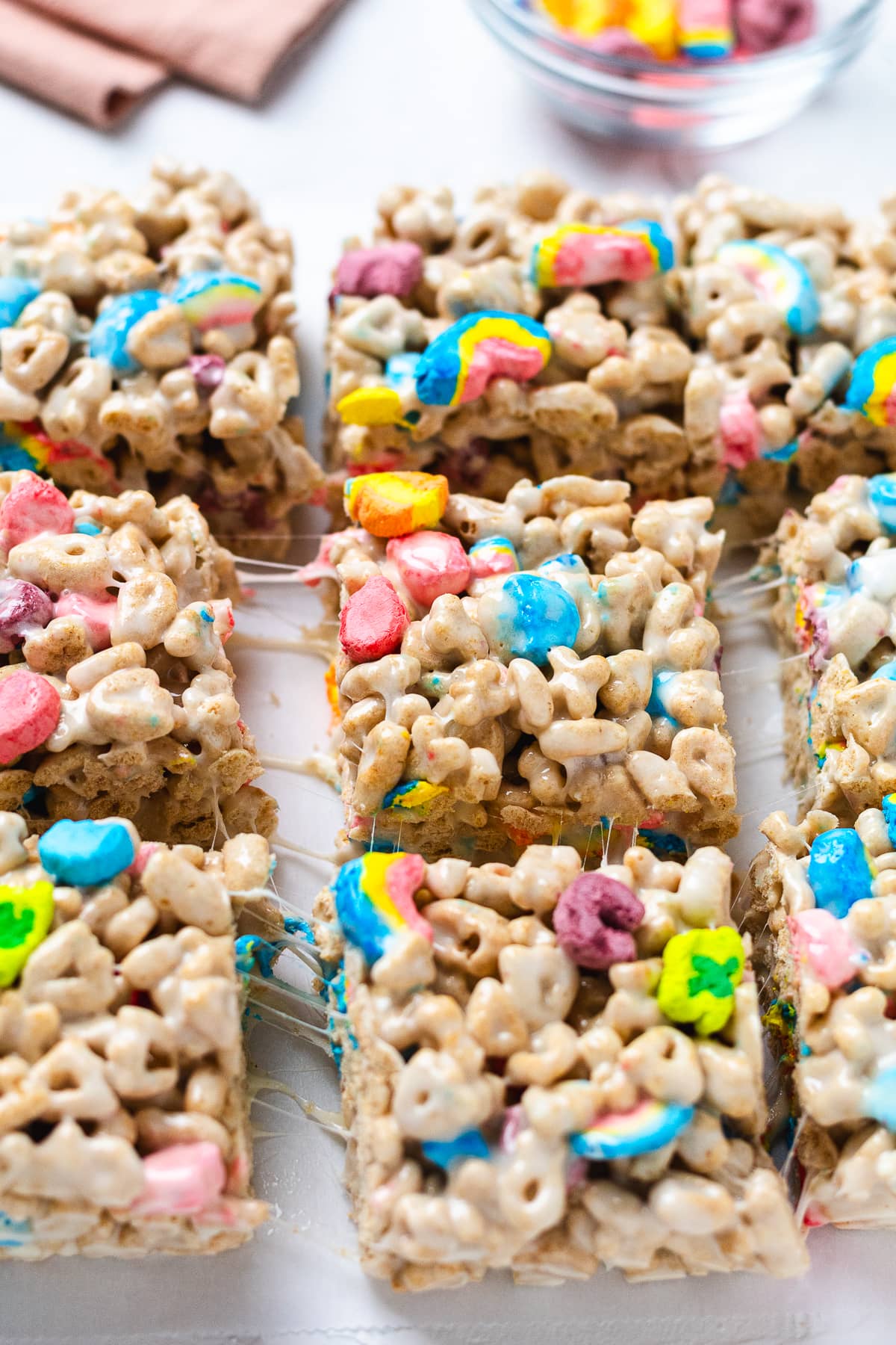 Rows of Lucky Charms marshmallow treats cut into squares on parchment paper.