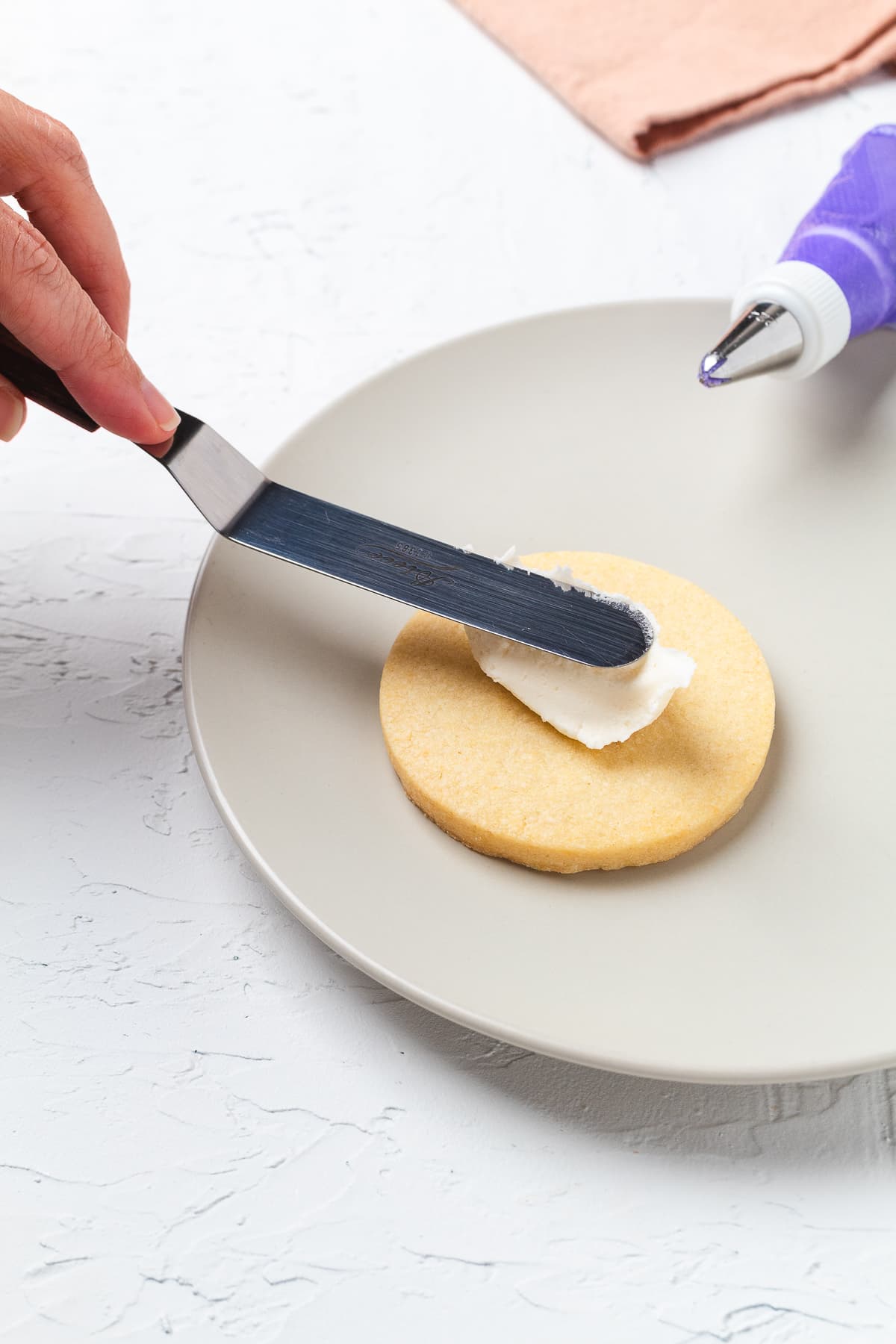 Spreading white frosting on round sugar cookie with offset spatula before decorating.