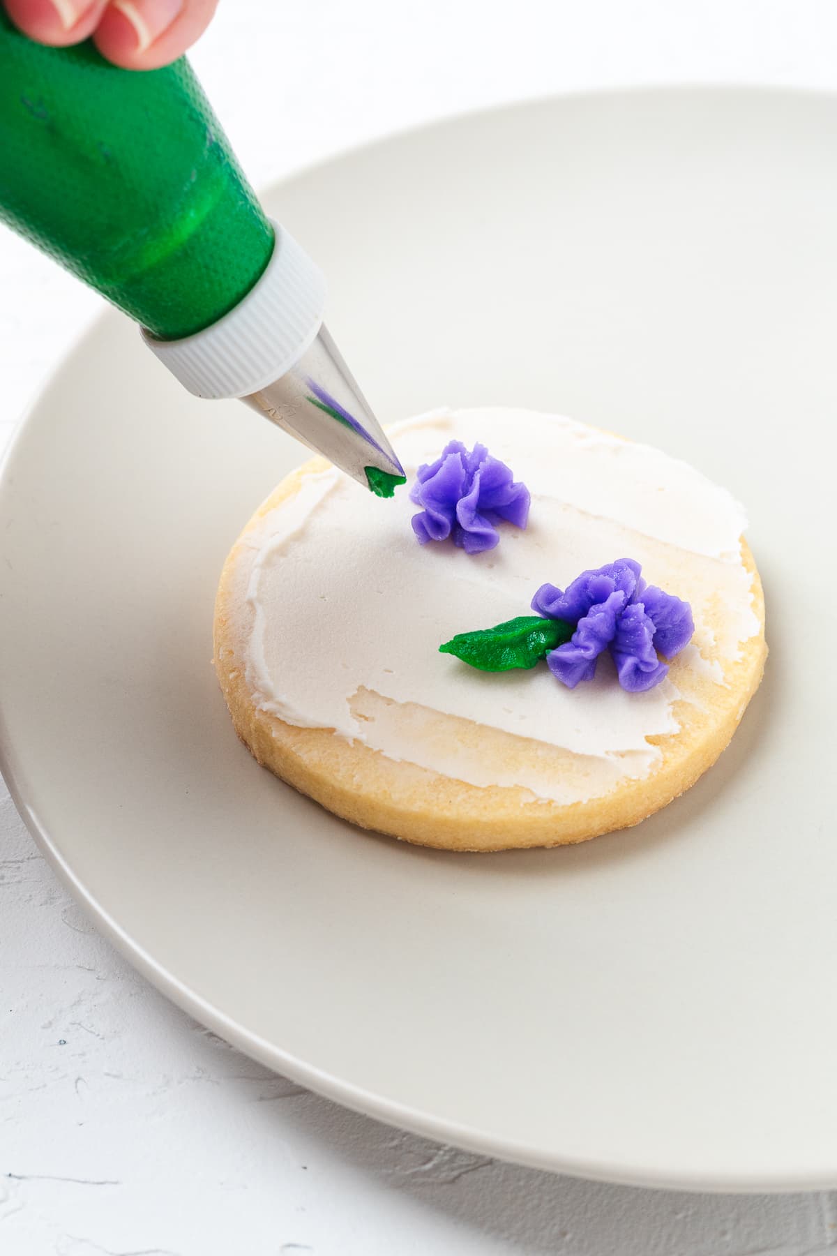 Adding green frosting leaves to purple flower buttercream on cookie.