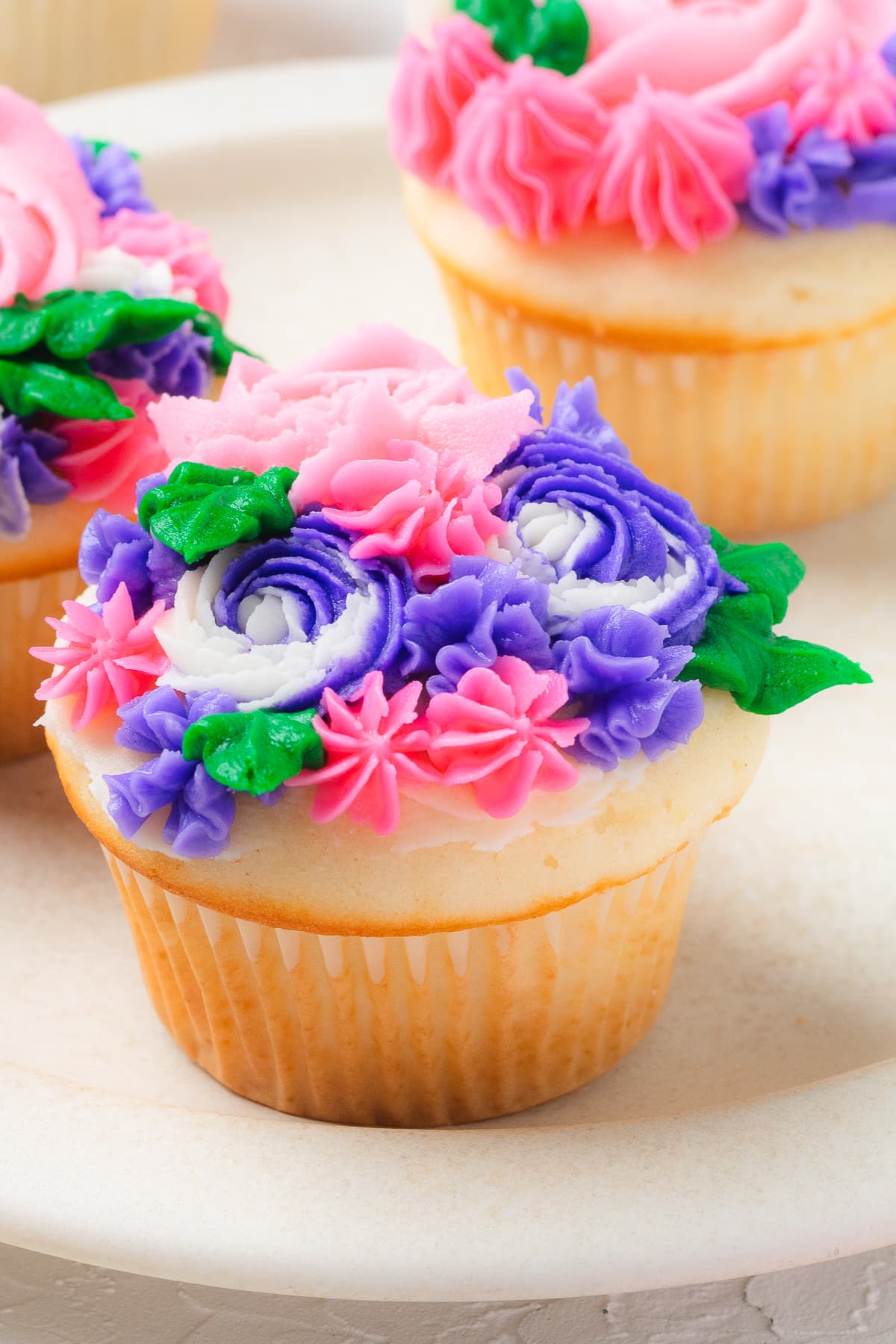 Cupcake decorated with pink, purple, and green buttercream flowers on white plate