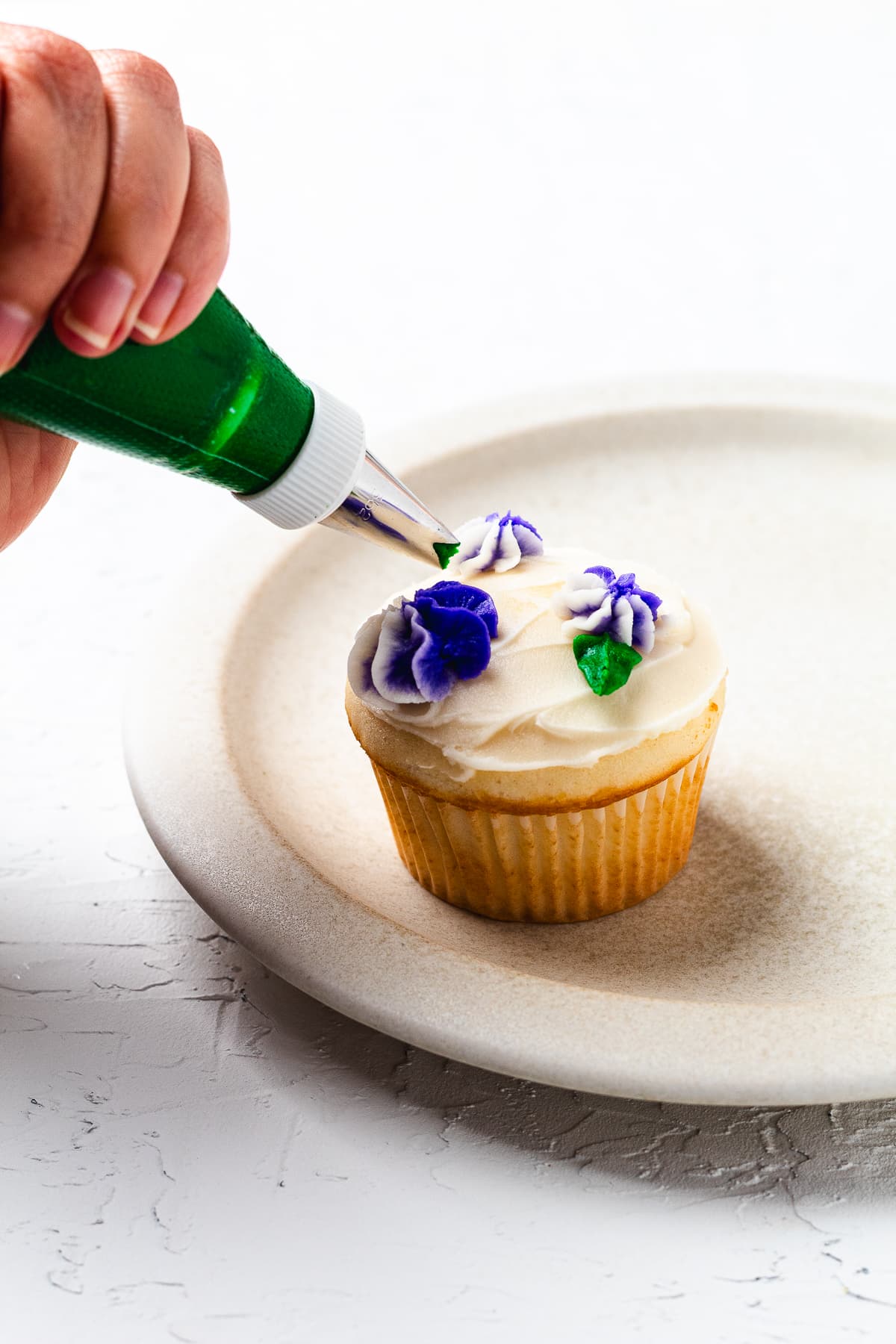 Adding green buttercream leaves to purple flower cupcake decoration.