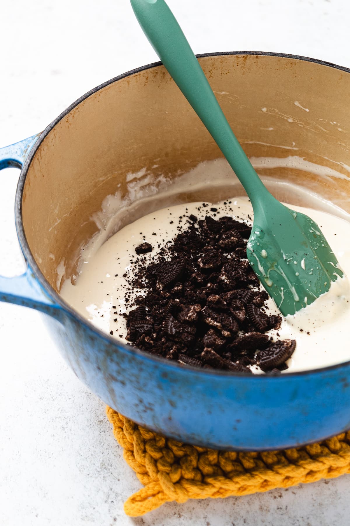Crushed Oreos being added to melted marshmallow mixture in a blue pot.