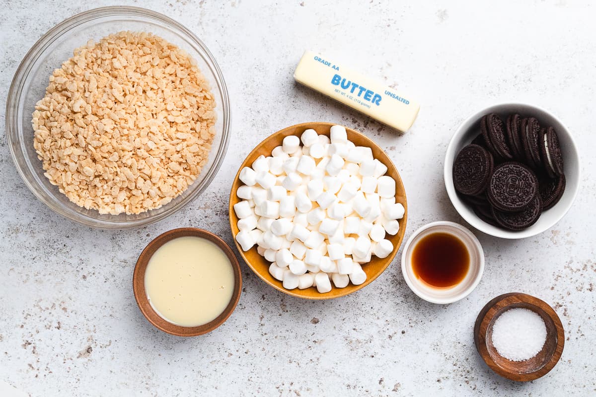 Bowls of ingredients for Oreo Rice Krispie treats including cereal, marshmallows, butter, Oreos, and vanilla.
