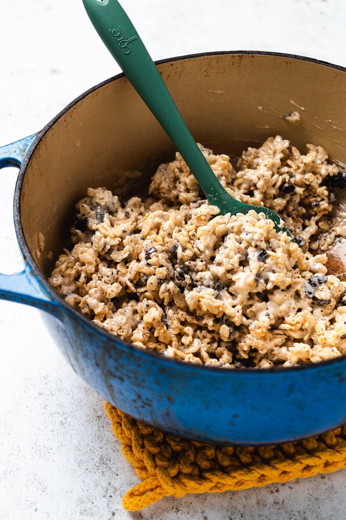 Pot filled with mixed Oreo Rice Krispie treat mixture being stirred with a green spatula.