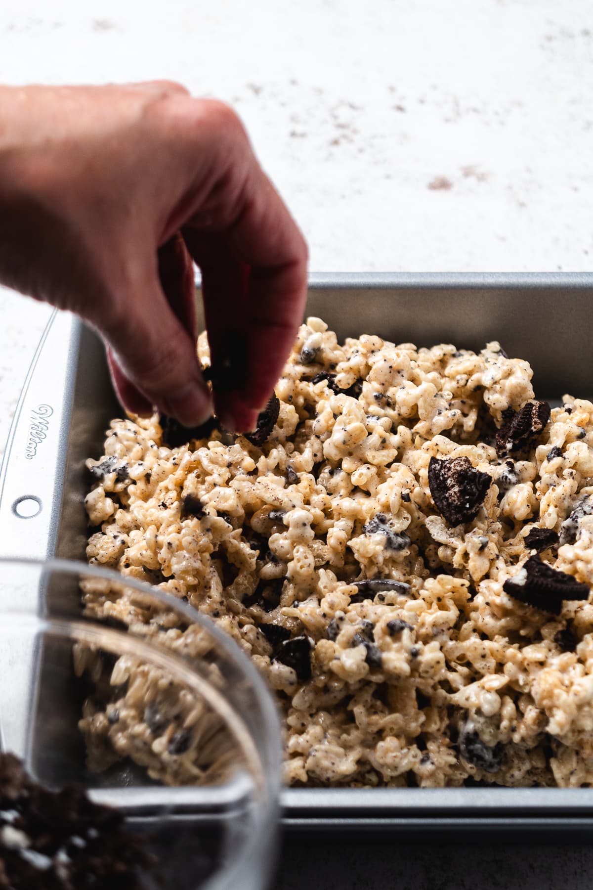 Hand pressing Oreo Rice Krispie mixture into a metal baking pan to set.