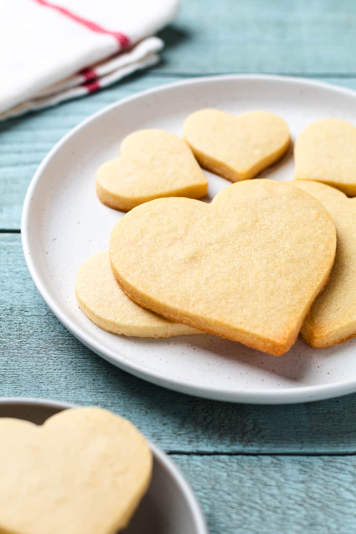 Baked heart-shaped sugar cookies cooling on a plate.