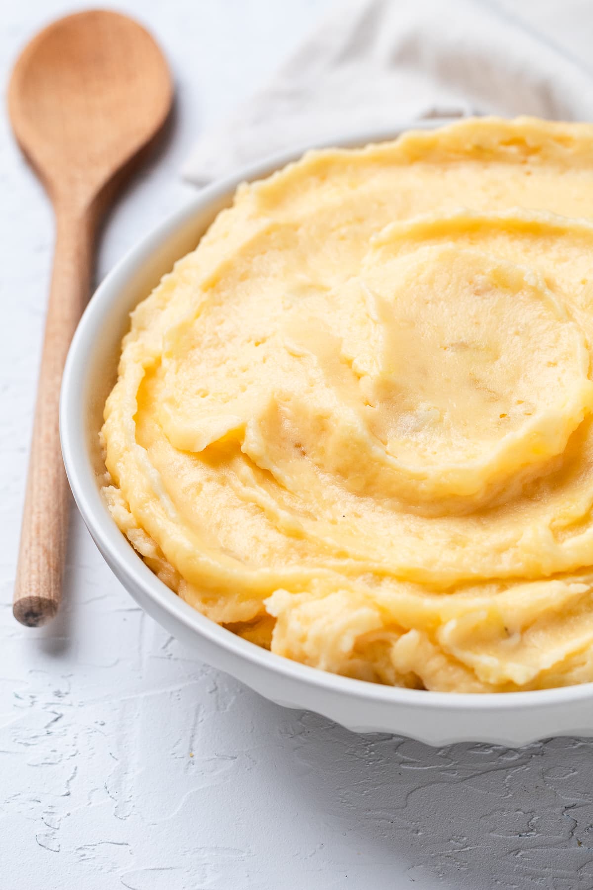 Bowl full of creamy, rustic, cheesy mashed potatoes in a white bowl with a wooden spoon.