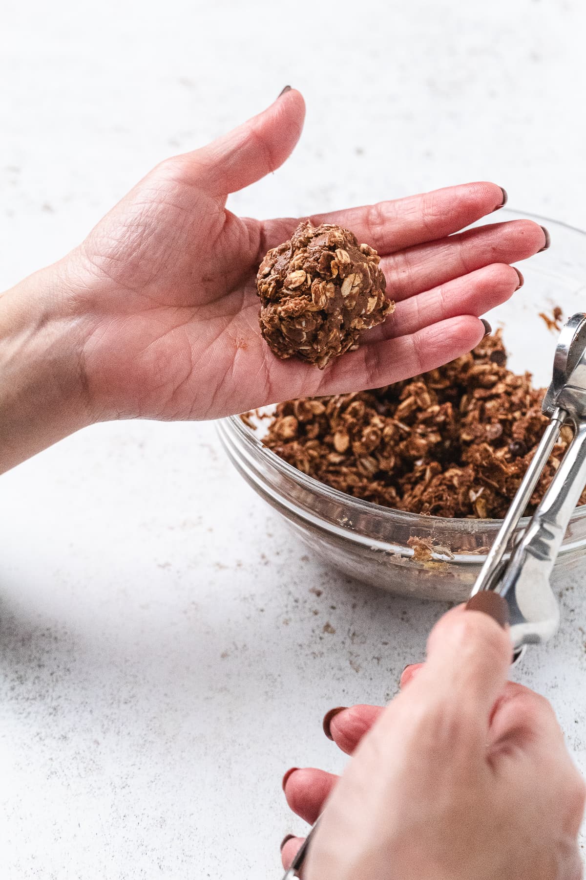 Hand rolling a chocolate protein ball mixture into a round ball over a glass bowl.
