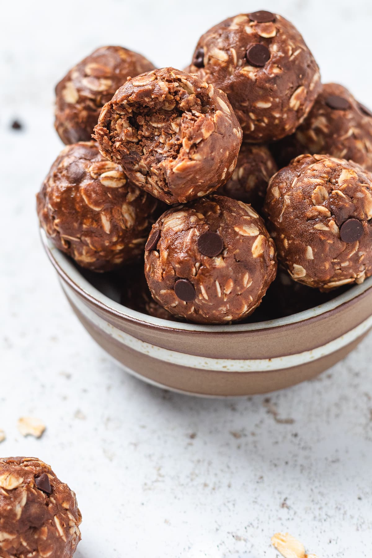 Bowl stacked with chocolate protein balls, one showing a bite revealing the soft texture.