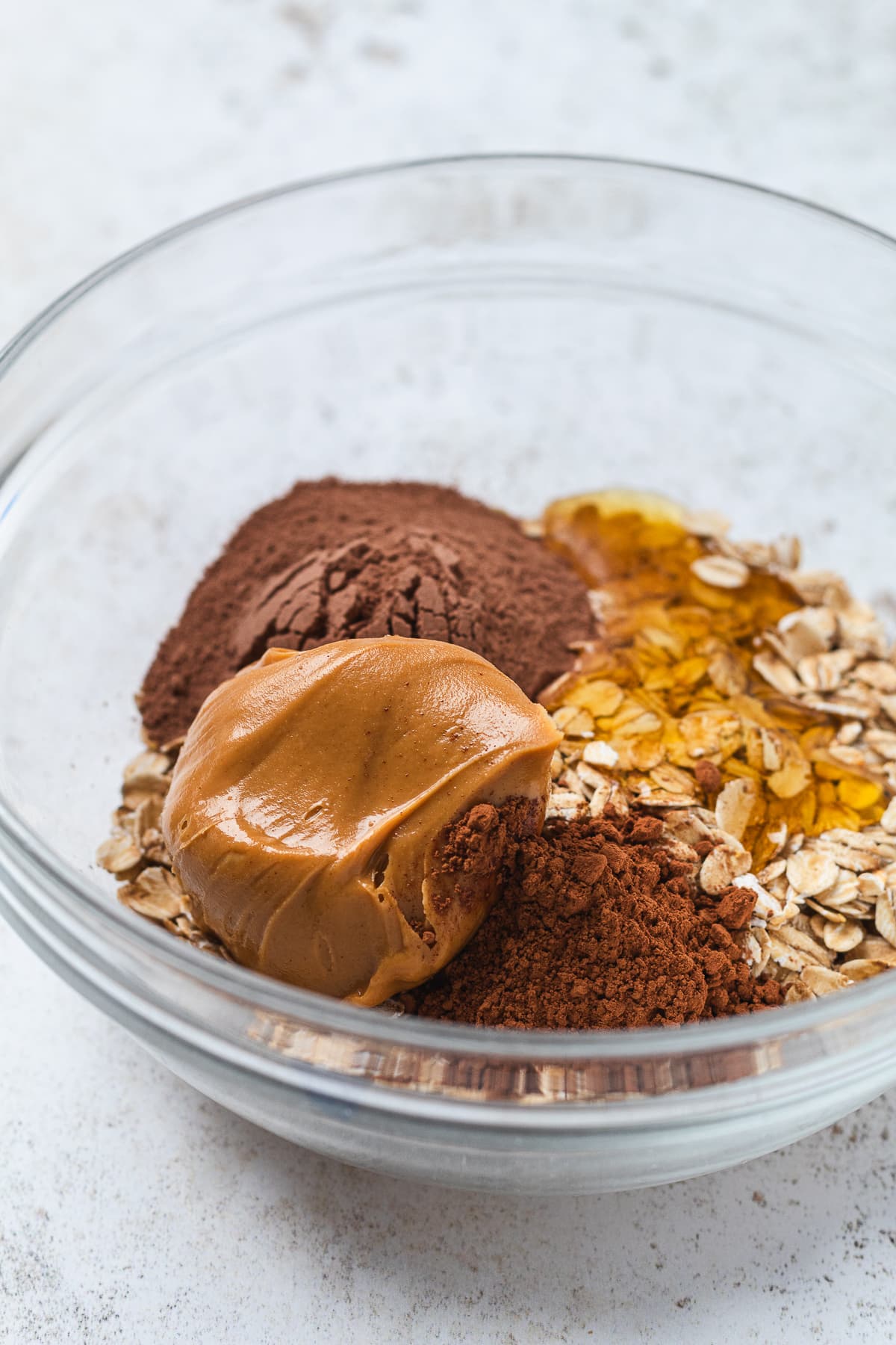 Chocolate protein ball ingredients added to a glass mixing bowl before stirring.