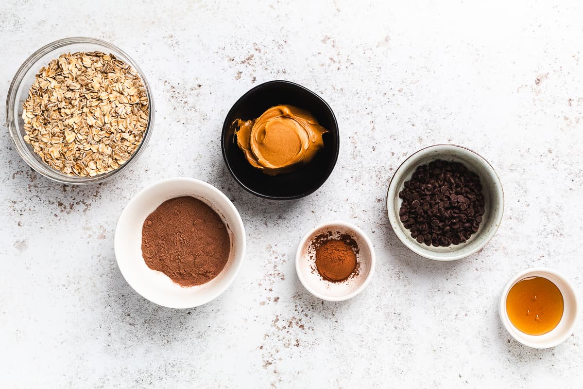 Ingredients for chocolate protein balls including oats, peanut butter, cocoa powder, cinnamon, chocolate chips, and honey.