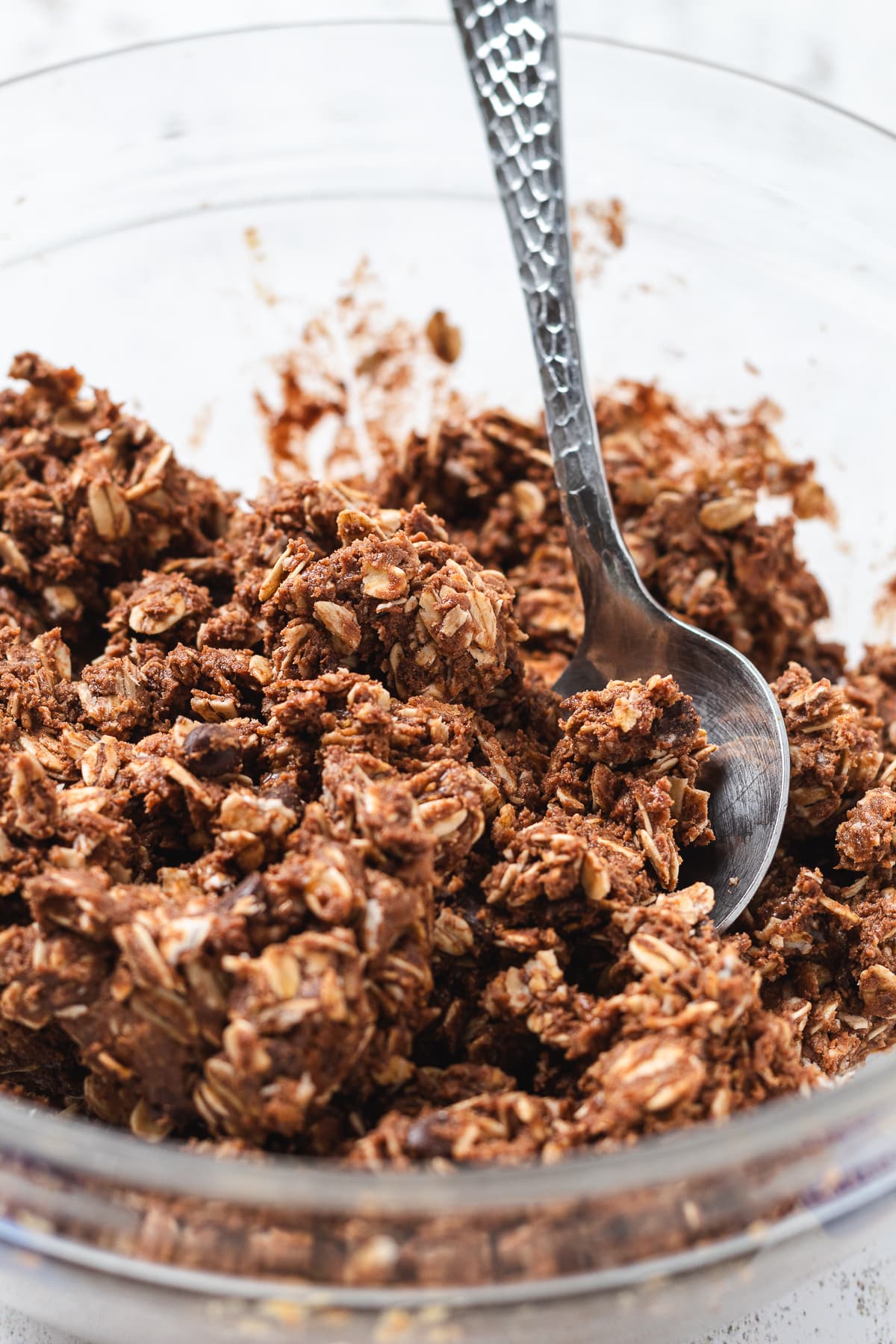 Chocolate protein ball mixture being stirred in a glass bowl.
