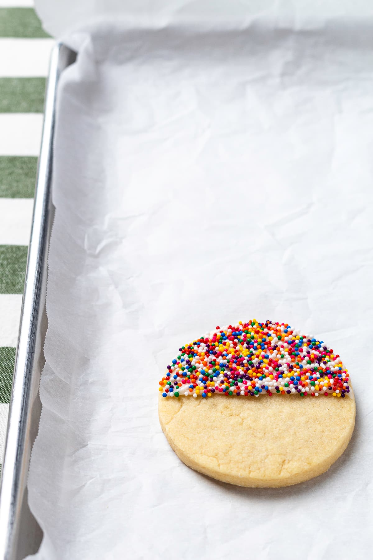 Cookie with half covered in rainbow sprinkles on baking sheet.