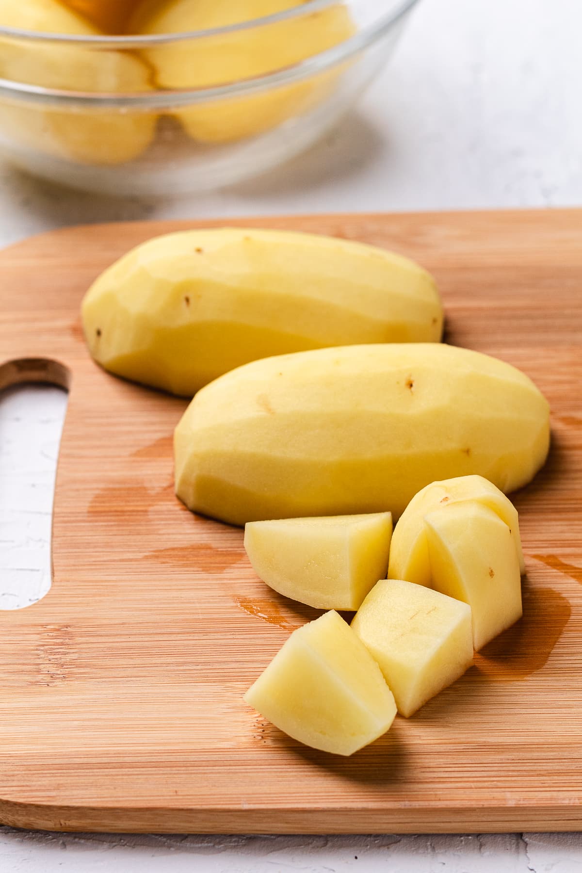 Peeled Yukon gold potatoes being cut into chunks on a wooden cutting board.