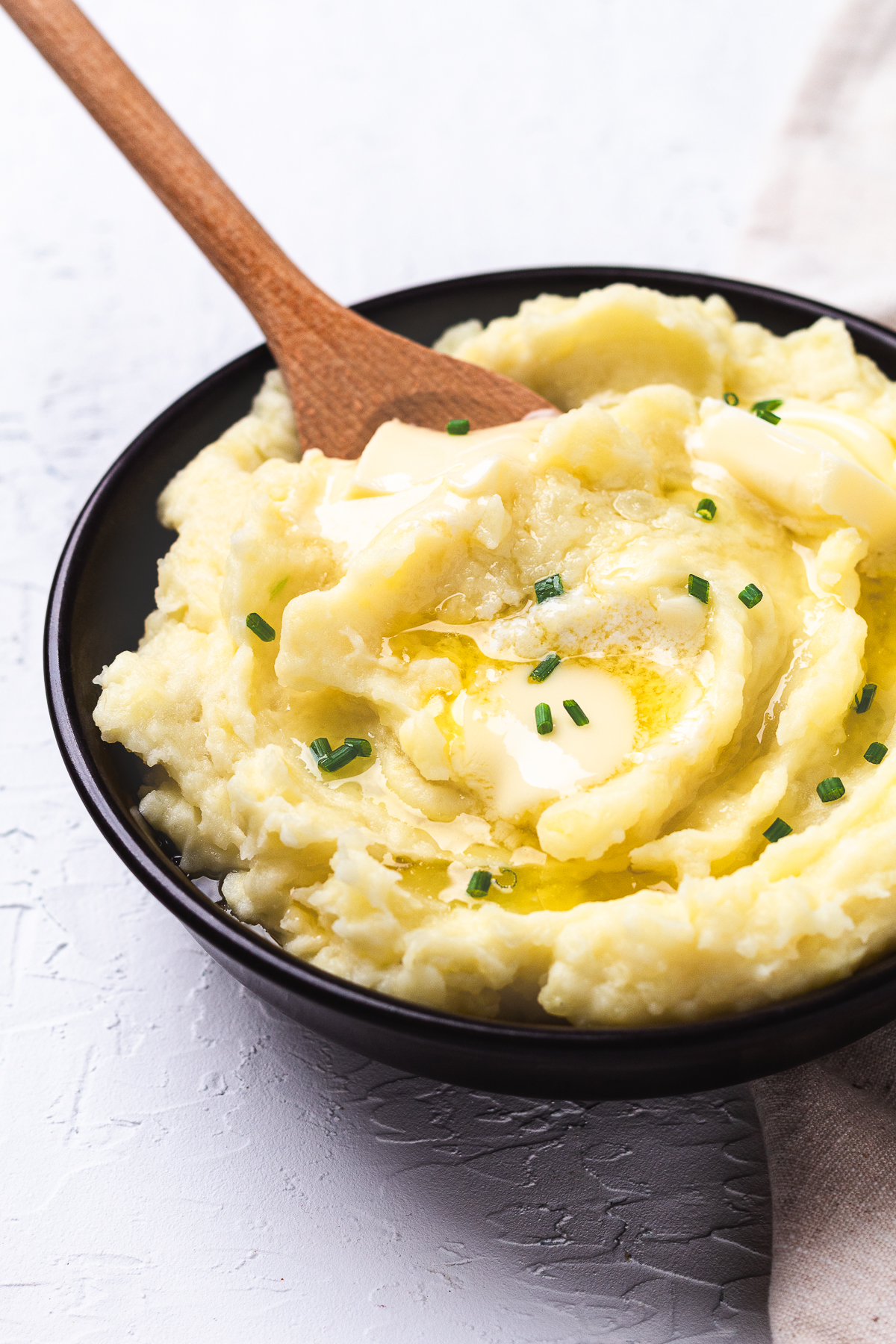 Close-up of creamy mashed potatoes with melted butter and chopped chives in a black bowl.