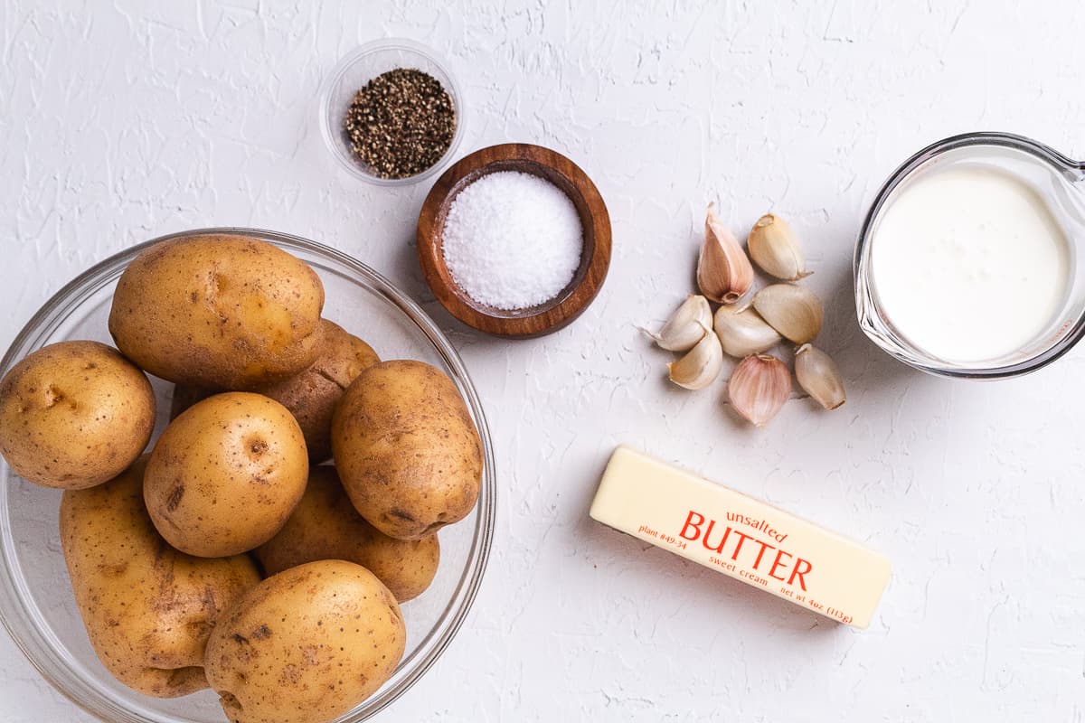 Yukon gold potatoes, butter, garlic, cream, salt, and pepper arranged on a white surface.