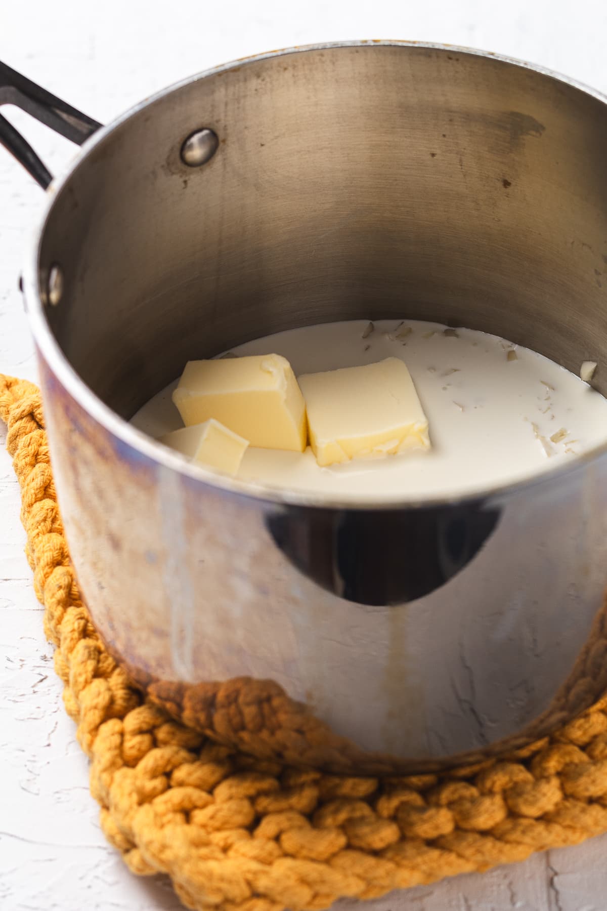 Butter melting in warm cream inside a stainless steel pot on a trivet.