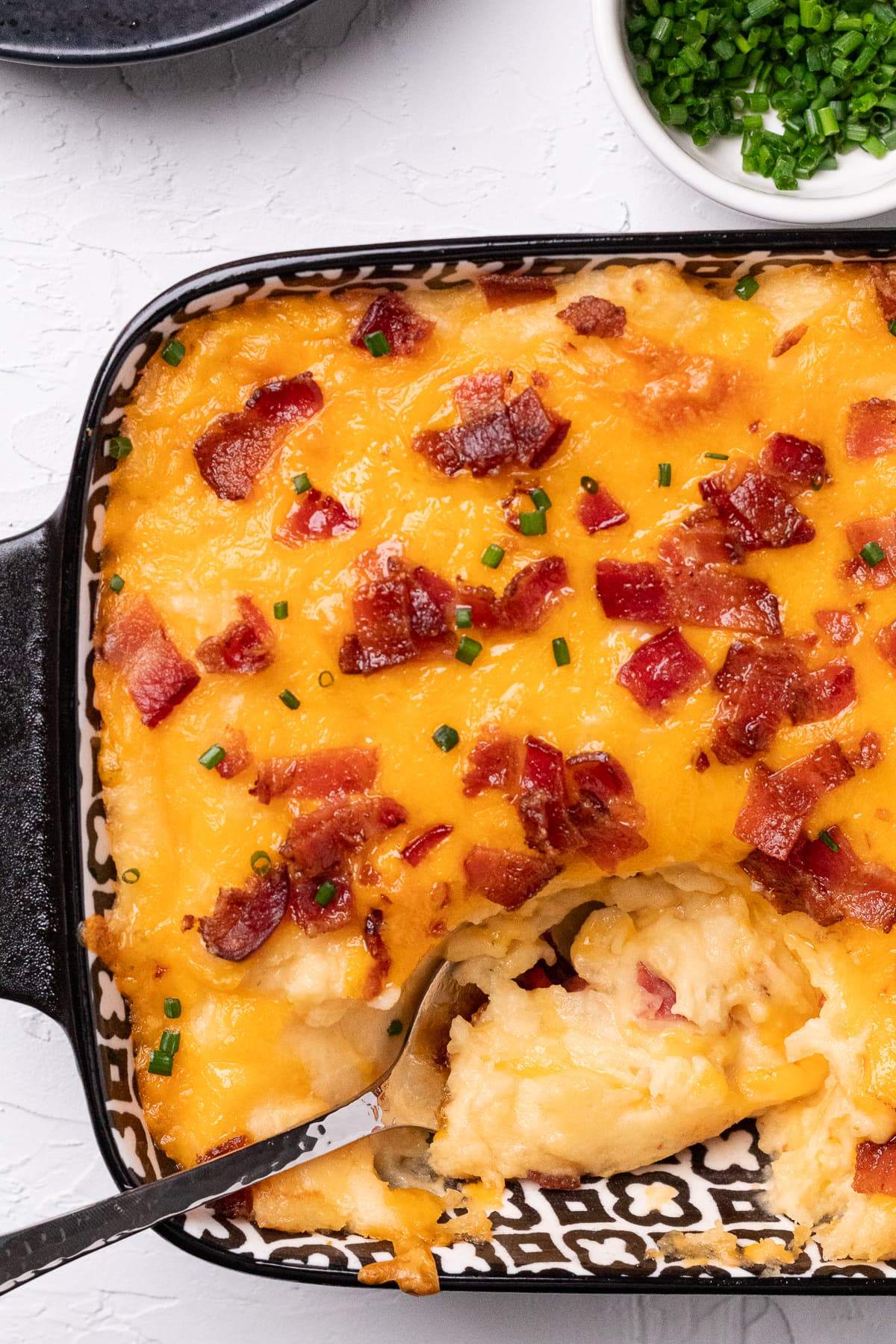 Spoonful of creamy loaded mashed potatoes with melted cheese and bacon scooped from casserole dish.