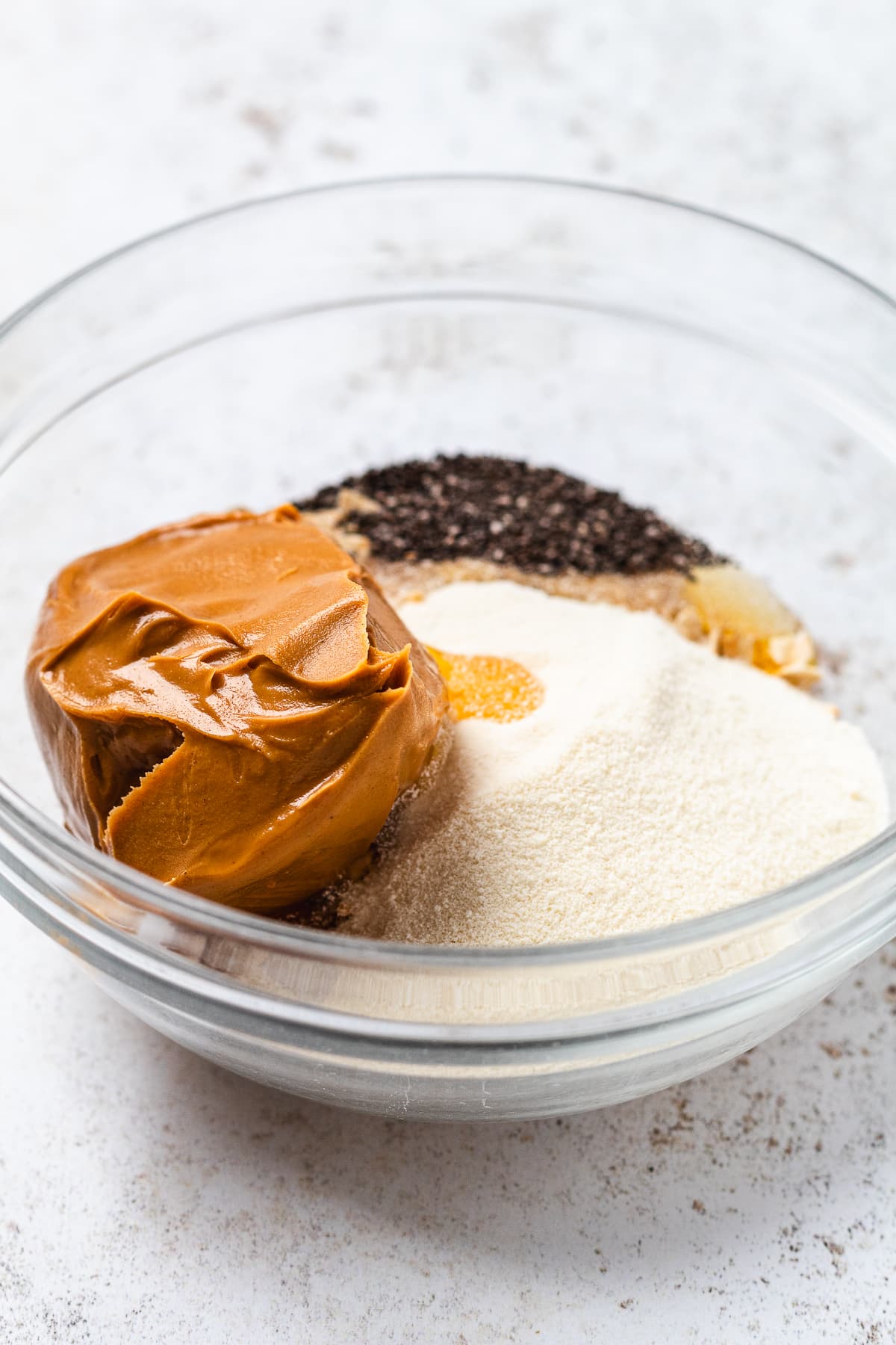 Bowl filled with peanut butter, chia seeds, protein powder, oats, and honey before mixing.