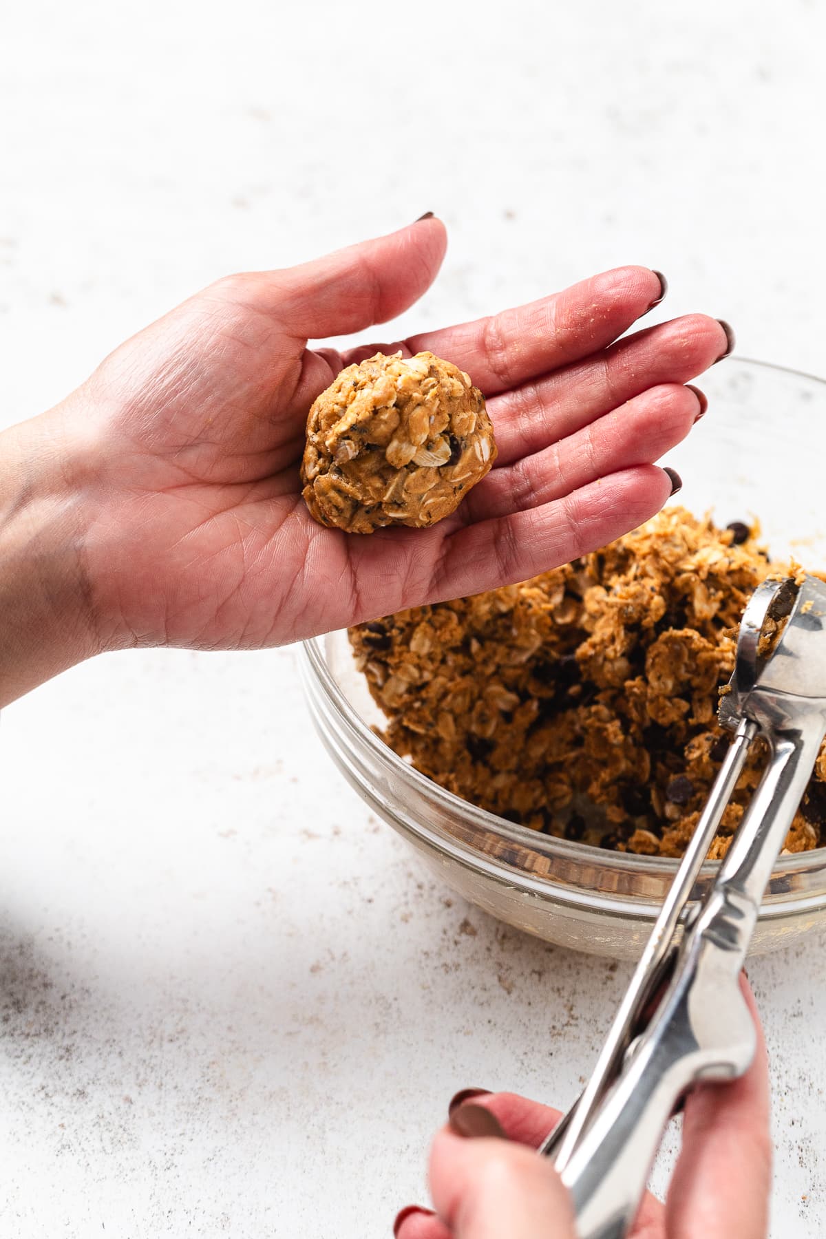 Hands scooping and shaping a no bake protein ball over a bowl of the mixture.