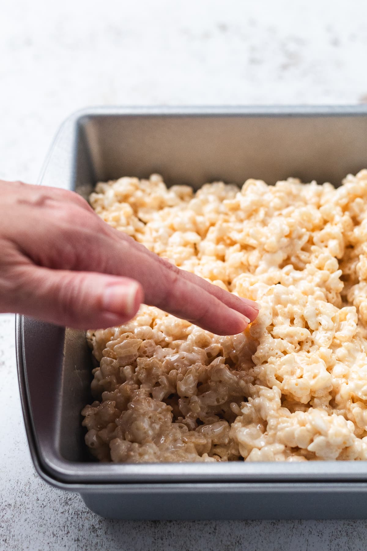 Hand pressing rice crispy mixture into a baking pan.
