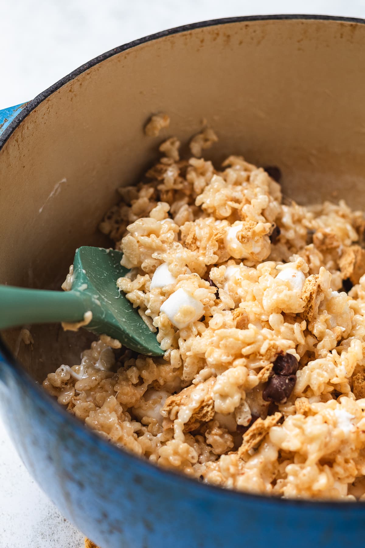 S’mores rice crispy mixture being stirred in a pot with graham crackers, marshmallows, and chocolate.