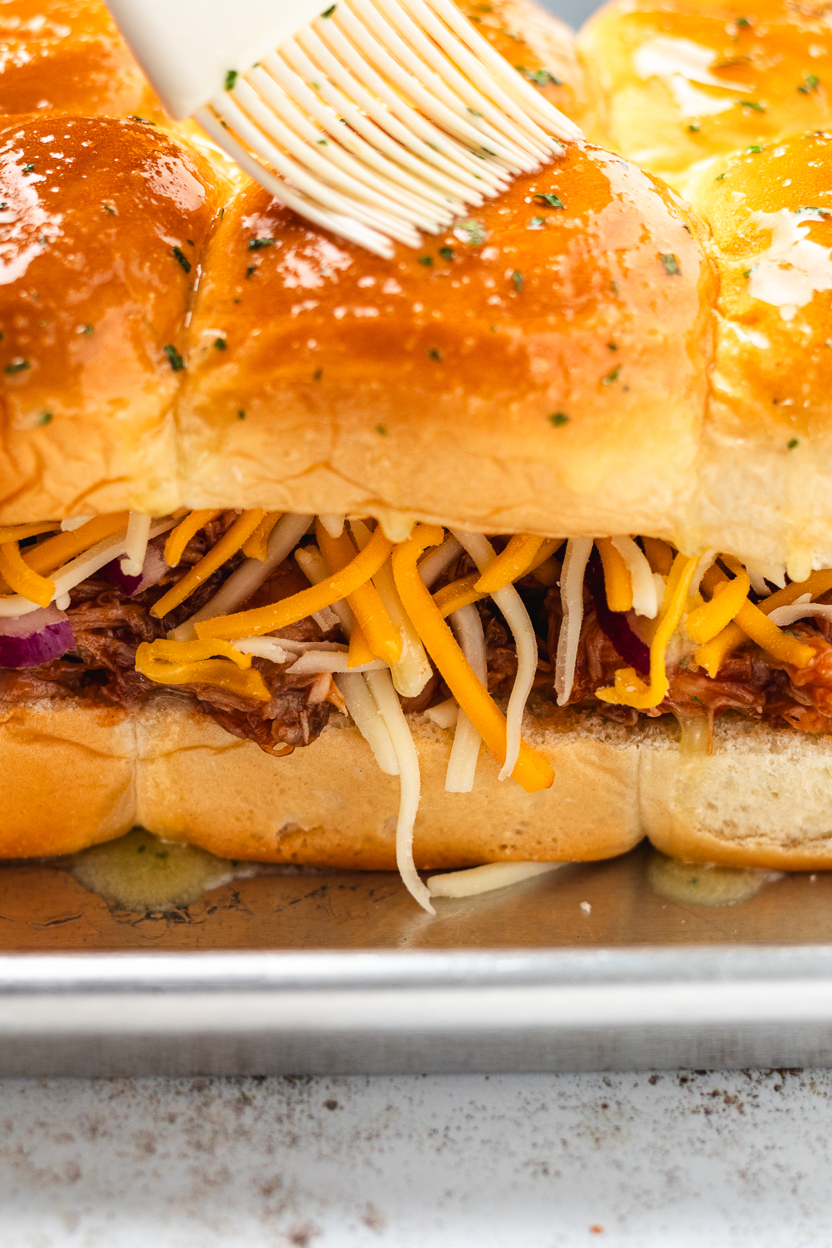 Herb butter brushed over the tops of BBQ chicken sliders filled with cheese and onions.