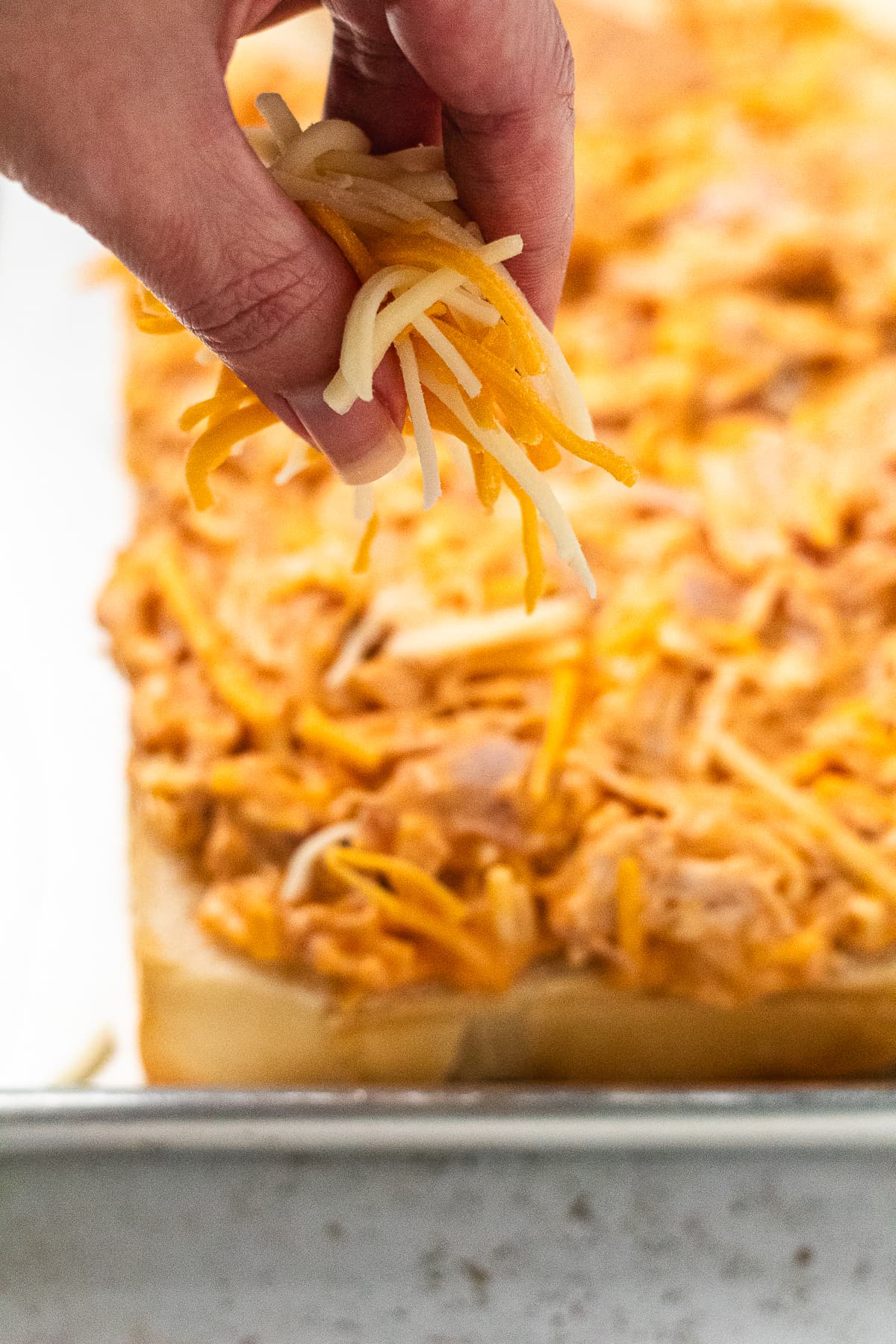 Hand sprinkling shredded cheese over buffalo chicken on Hawaiian rolls.