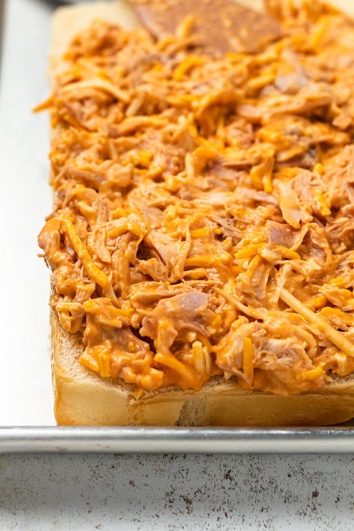 Shredded buffalo chicken mixture spread over sliced Hawaiian rolls before baking.