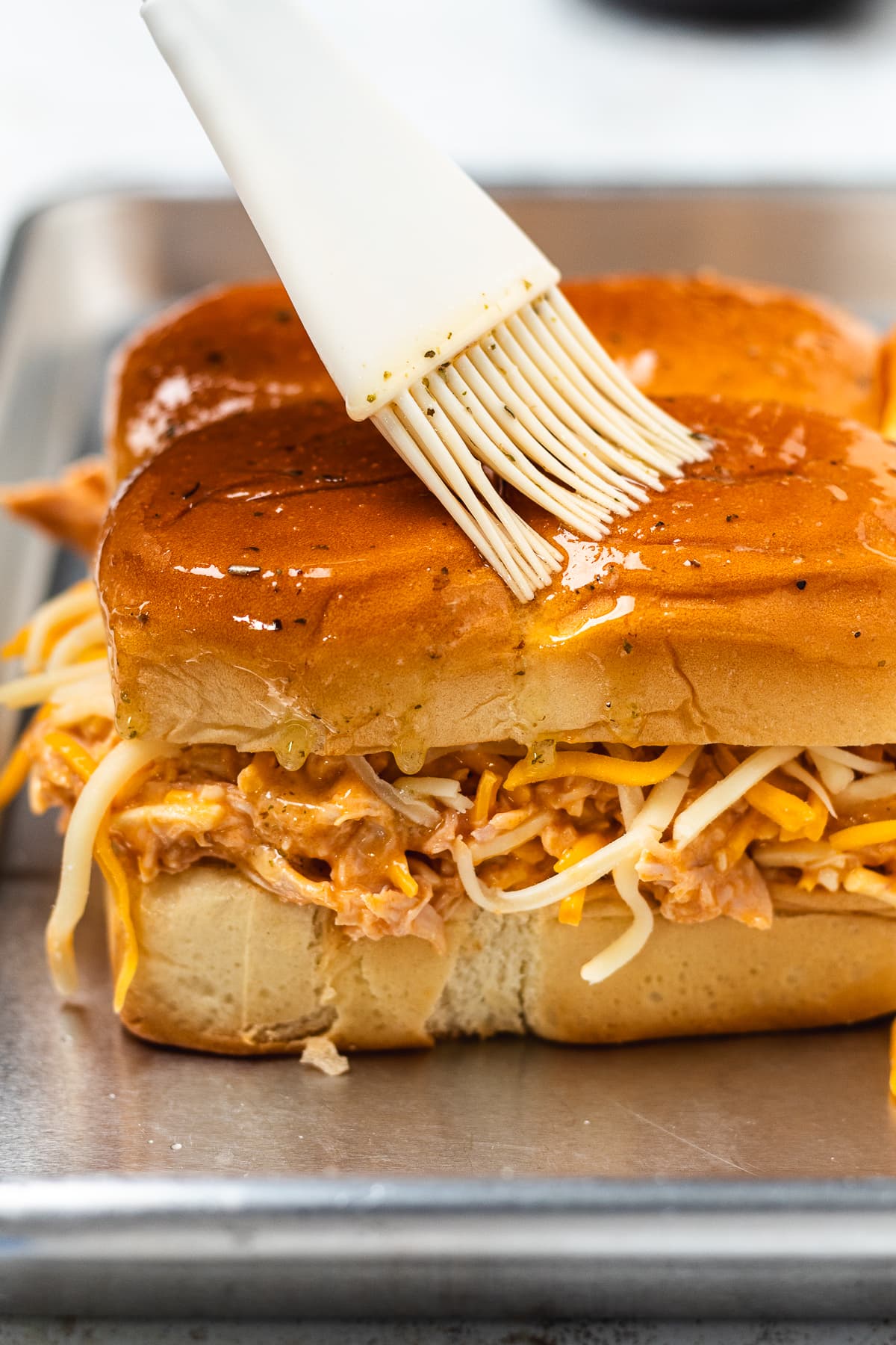 Herb butter being brushed onto the tops of assembled buffalo chicken sliders.