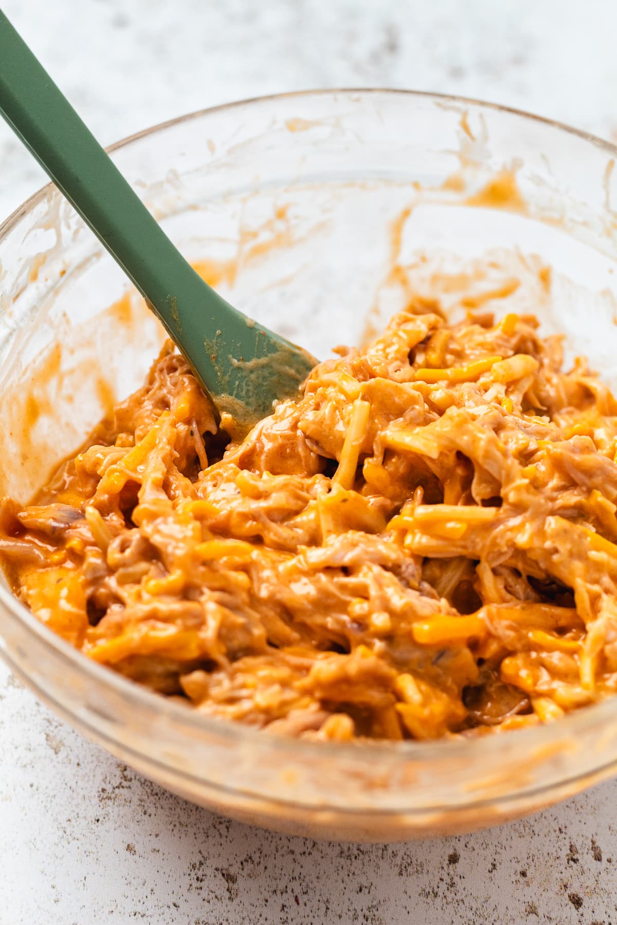 Bowl of shredded buffalo chicken mixed with buffalo sauce, ranch, and cheese.