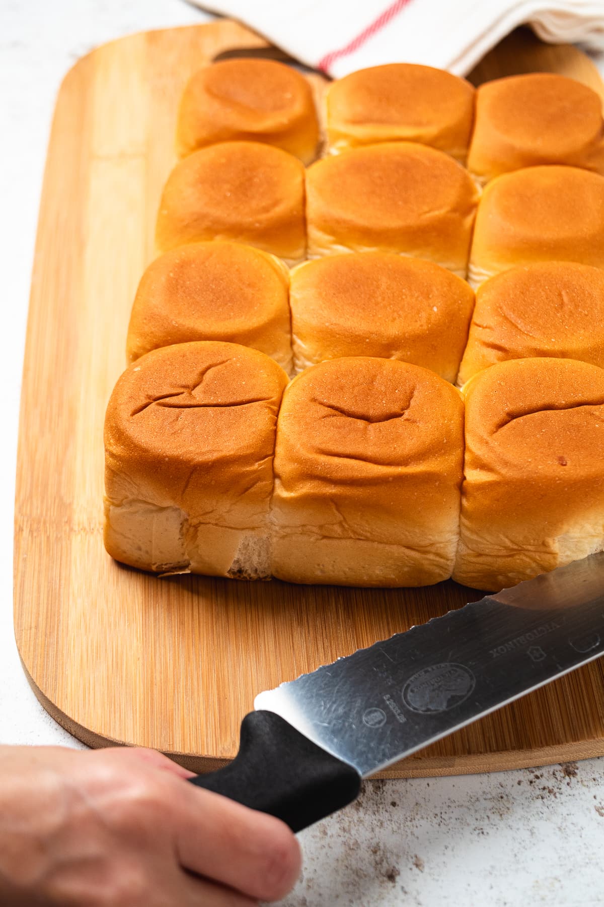 Hand holding a knife slicing rolls on a cutting board.