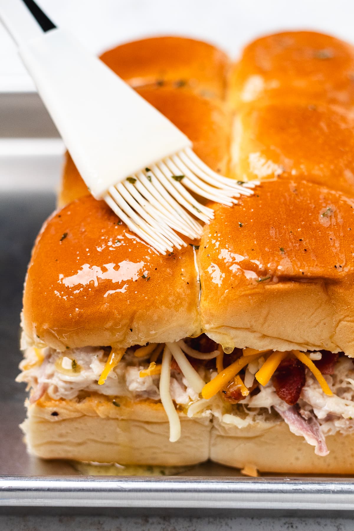 Herb butter being brushed over the tops of assembled chicken bacon ranch sliders.