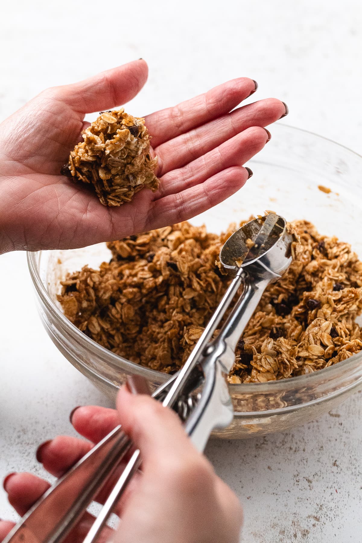 Hand holding a scoop of banana oat mixture while forming a protein ball.