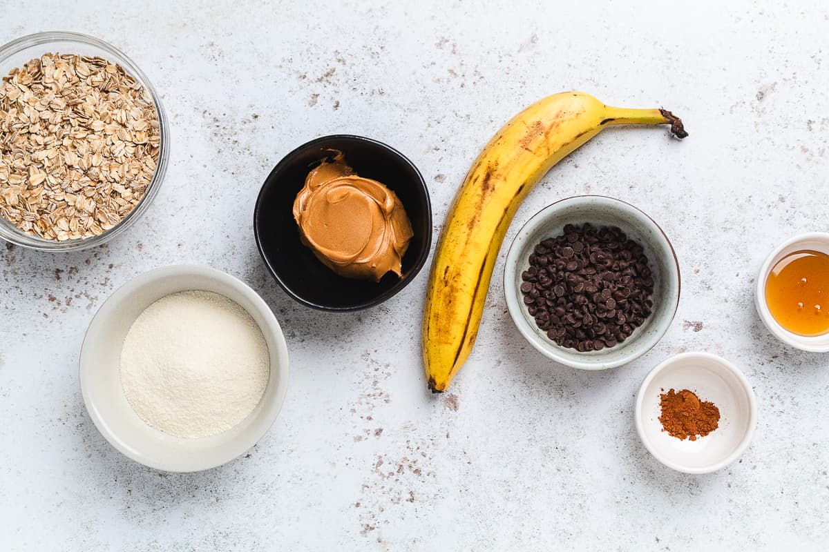 Ingredients for banana protein balls arranged on a counter, including oats, banana, peanut butter, chocolate chips, and honey.