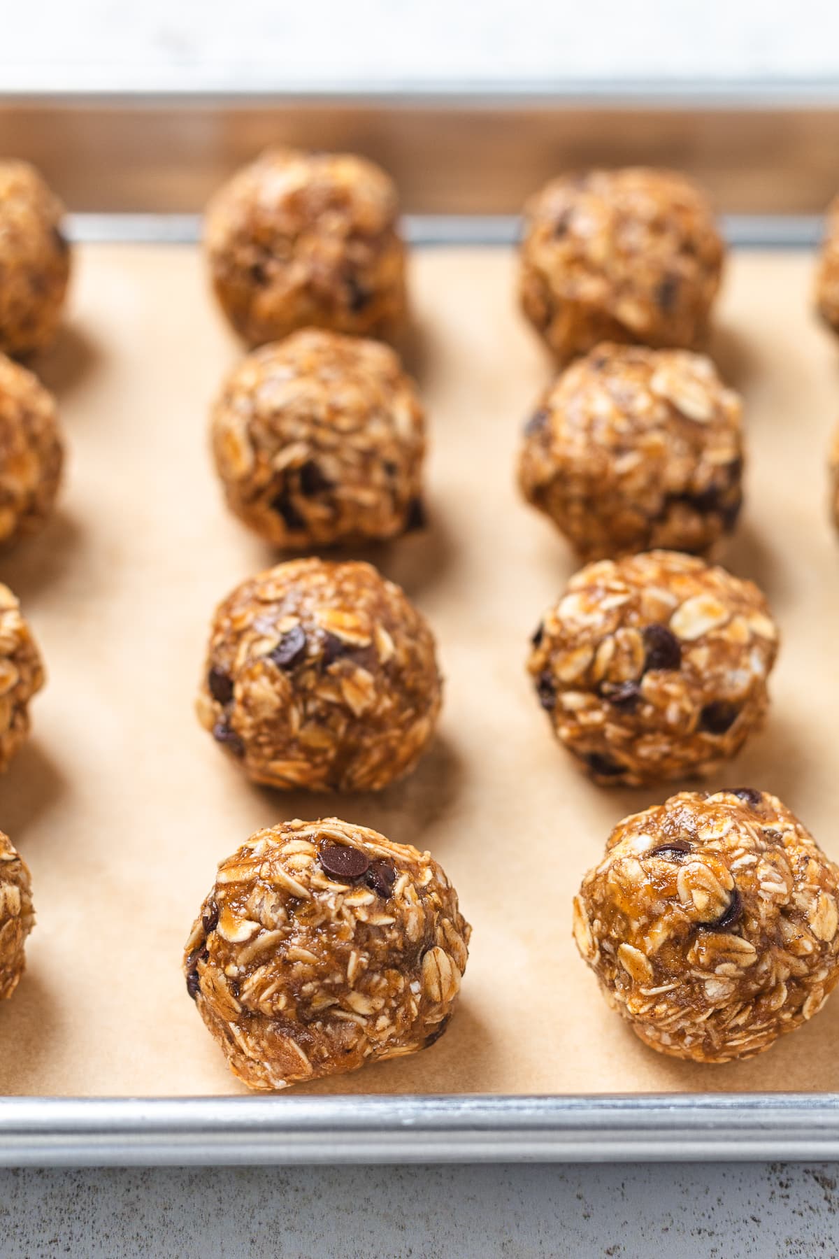 Rows of rolled banana protein balls chilling on a parchment-lined baking sheet.