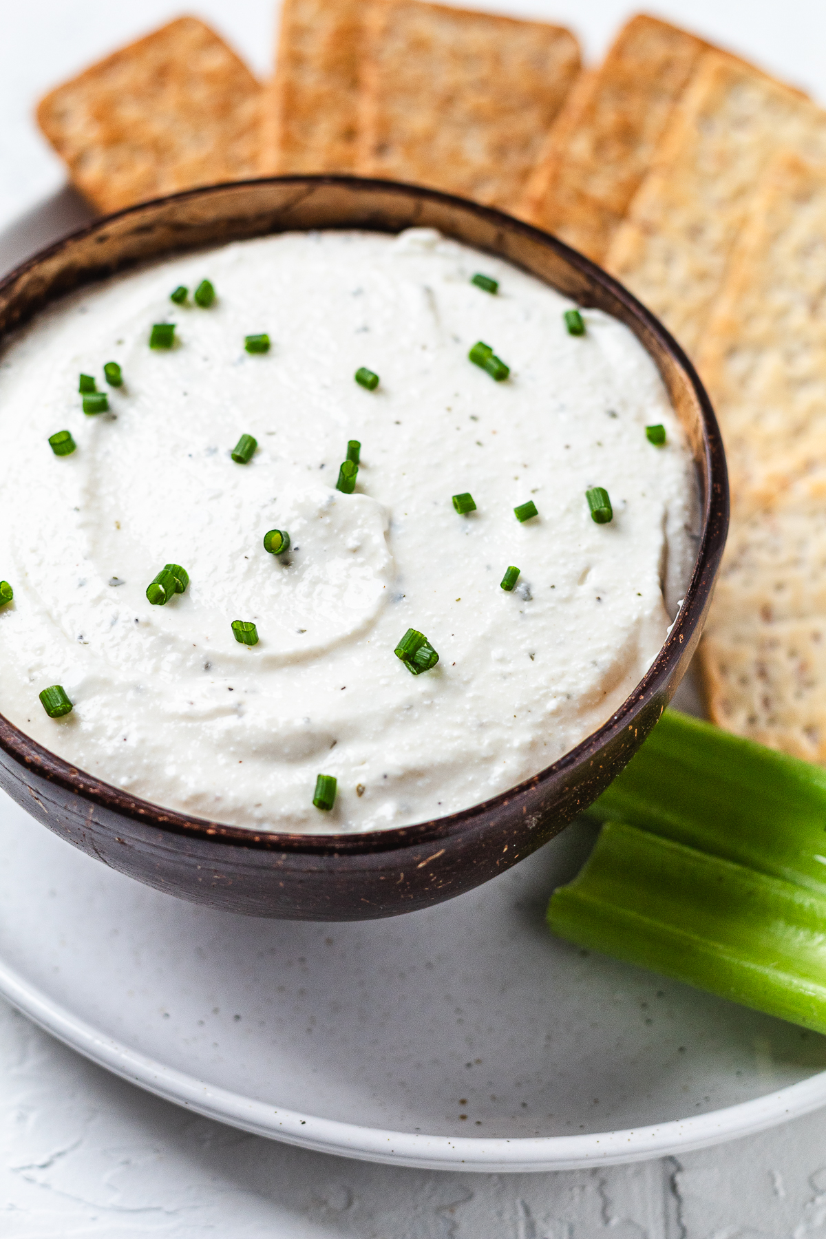 Bowl of creamy cottage cheese ranch dip garnished with chives, served with crackers and celery sticks.