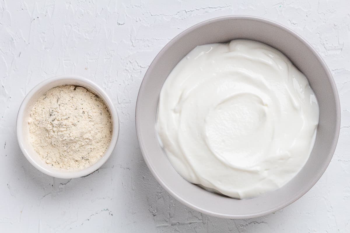 Small bowls of Greek yogurt and ranch seasoning displayed on a white surface.