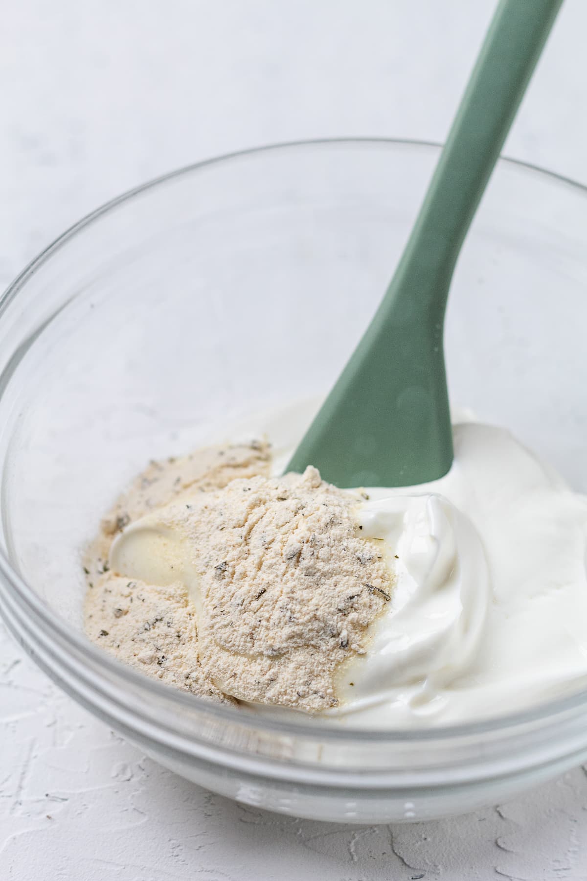 Ranch seasoning added to Greek yogurt in a glass bowl, ready to be mixed into a protein dip.