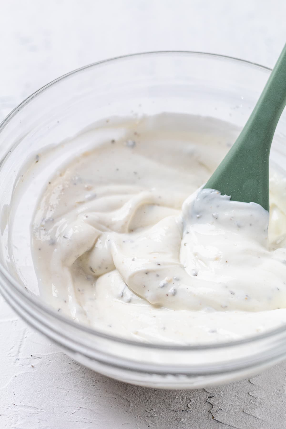 Greek yogurt ranch dip being stirred in a glass bowl until smooth and creamy.