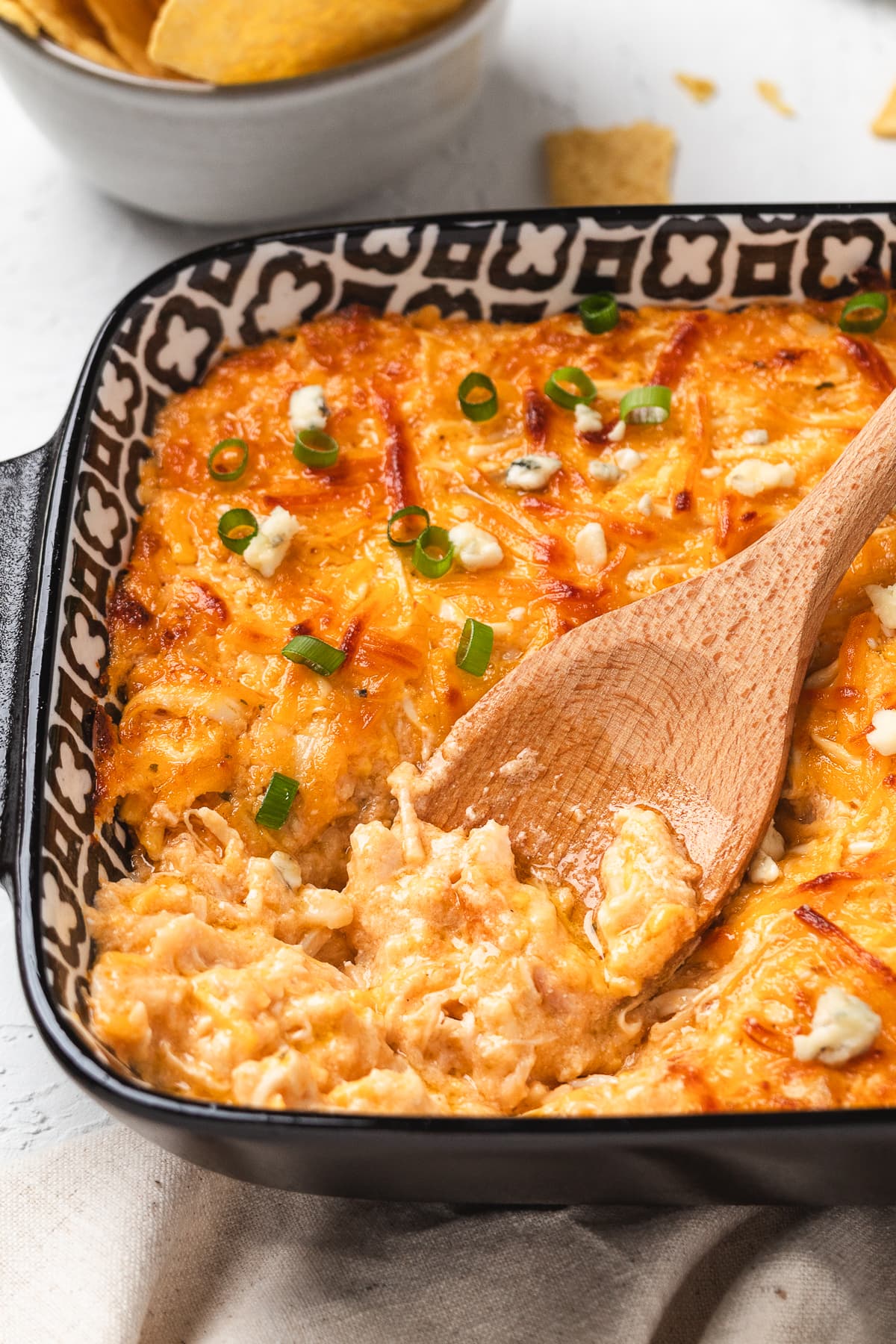 Spoon scooping creamy buffalo chicken dip from a hot baking dish.