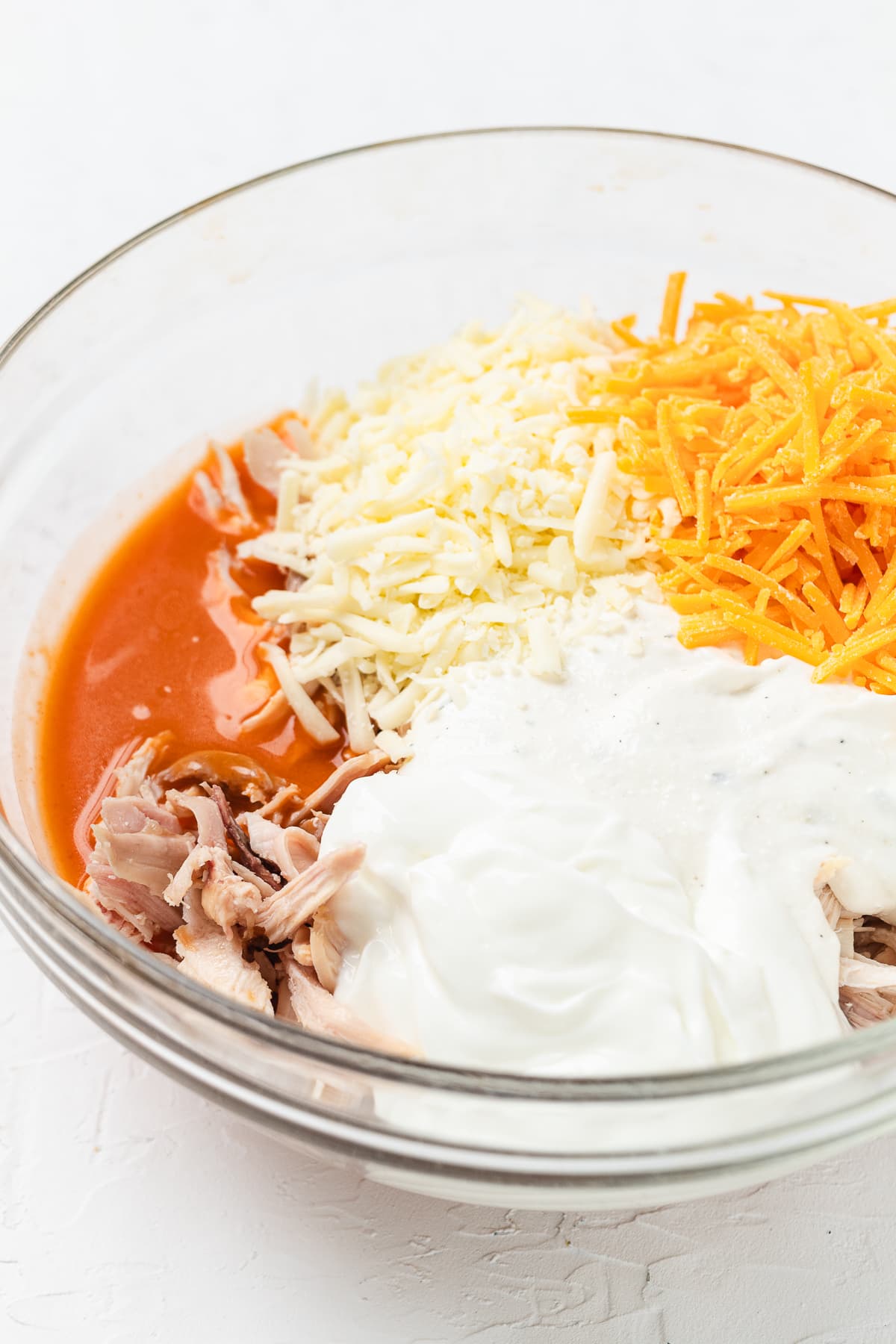 Buffalo chicken dip ingredients in a bowl, including shredded chicken, cheeses, and hot sauce.