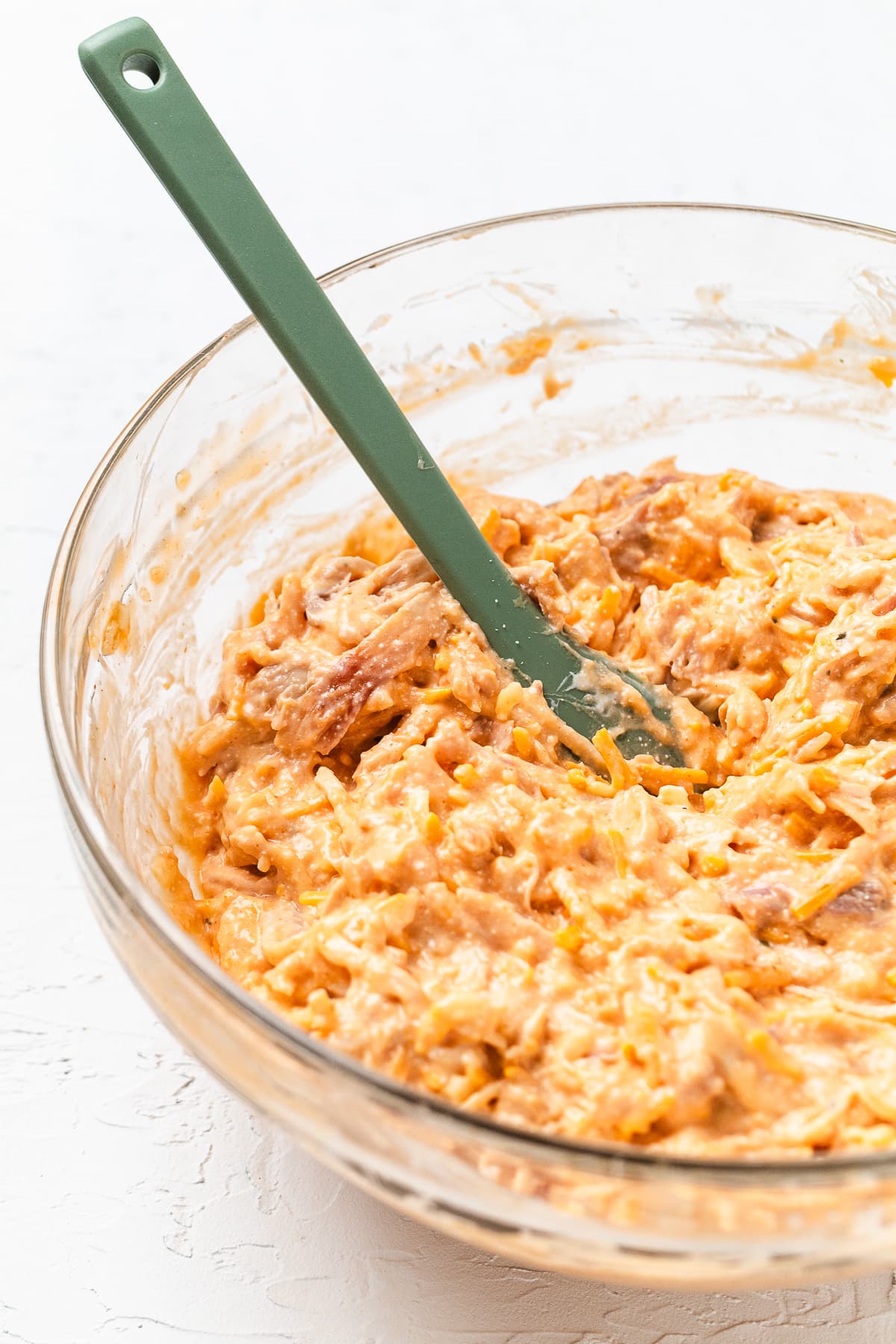 Buffalo chicken dip mixture stirred together in a glass bowl with a spatula.