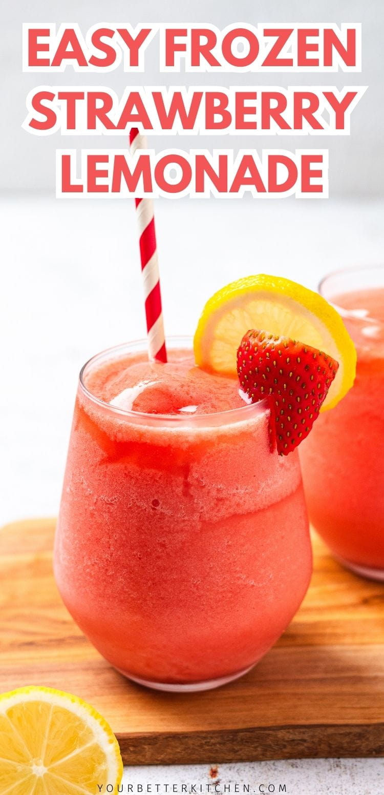 Glass of frozen strawberry lemonade with striped straw, lemon slice and strawberry garnish on a wooden board.