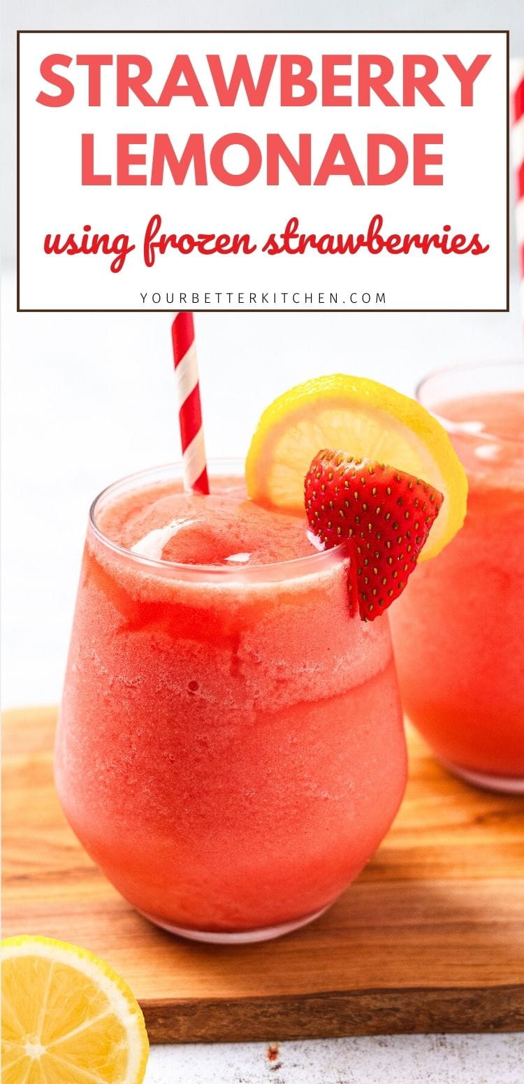 Glass of frozen strawberry lemonade with striped straw, lemon slice, and strawberry garnish on a wooden board.