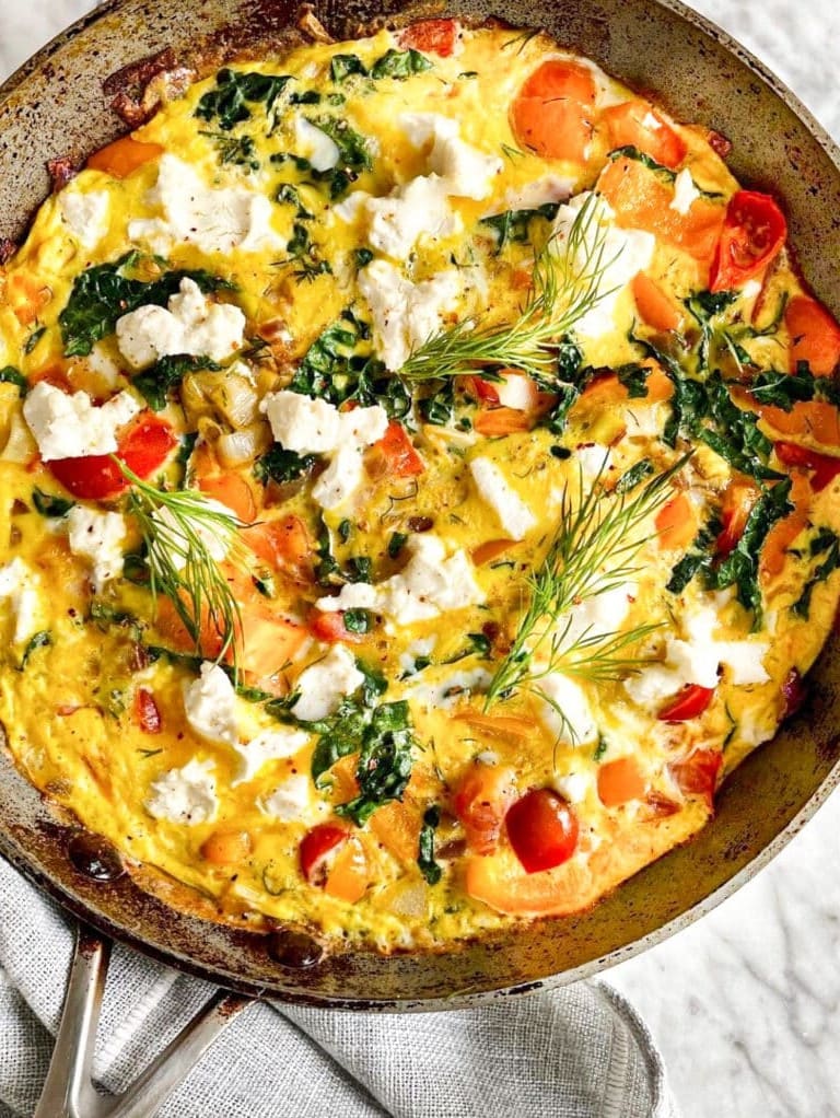 Vegetable frittata with tomatoes, greens, and cheese cooked in a skillet.